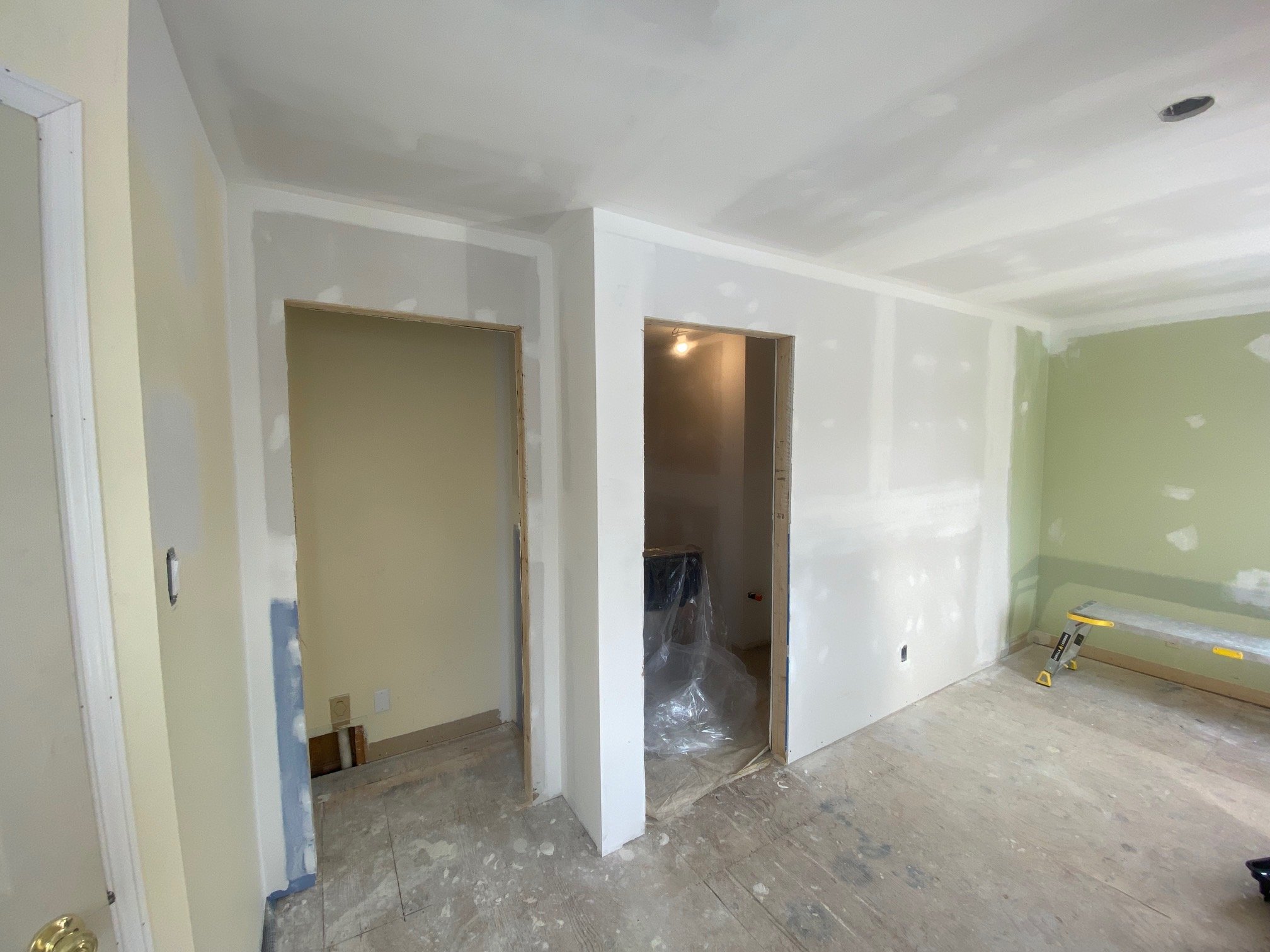 Interior of a house under renovation, with drywall installation in progress, and construction tools on the unfinished wooden floor.