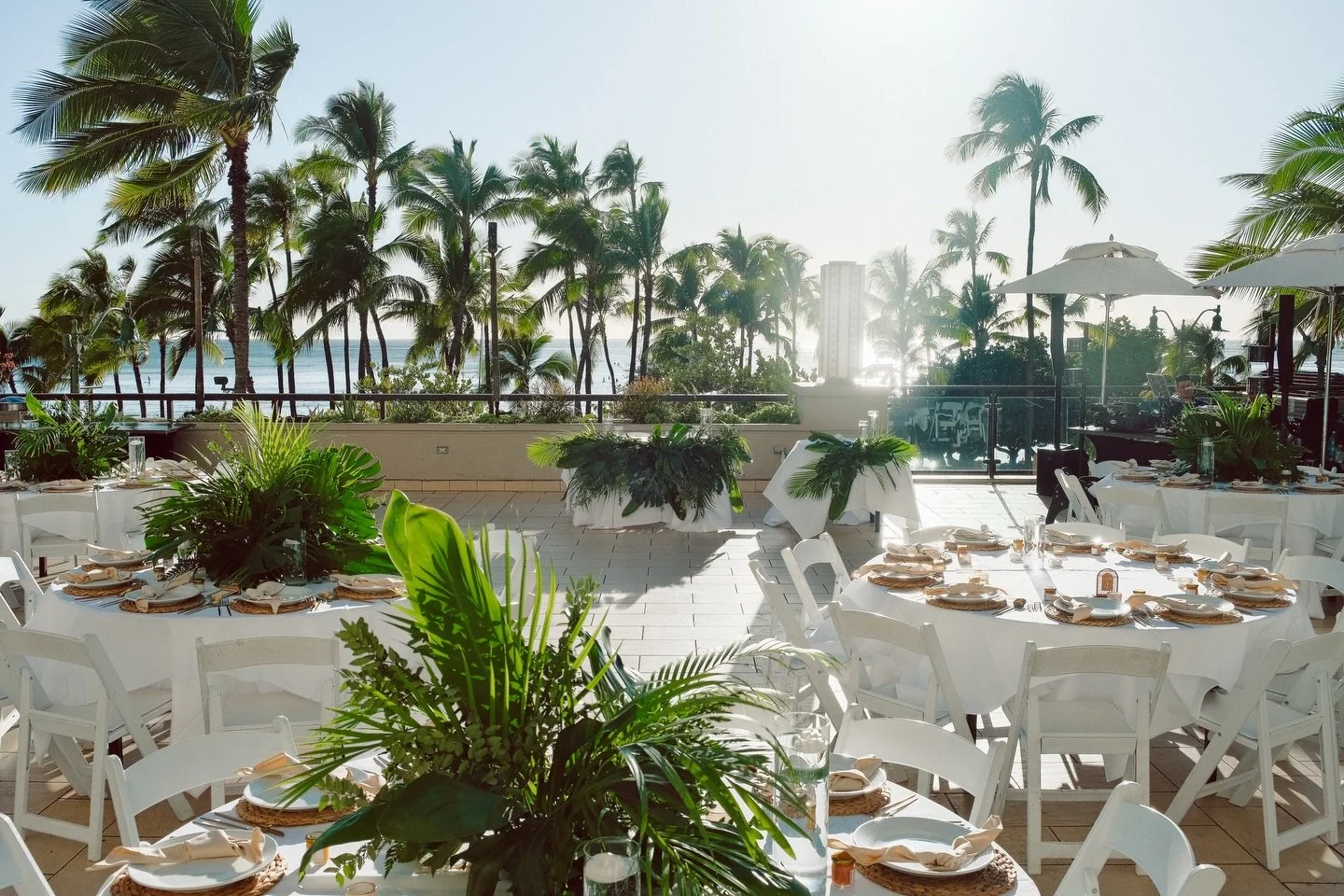 For this wedding we designed lush tropical centerpieces using layered greenery to complement the oceanfront views of Waikiki. The clean white tables, woven chargers, and soft neutral tones allowed the florals to stand out while keeping the overall lo