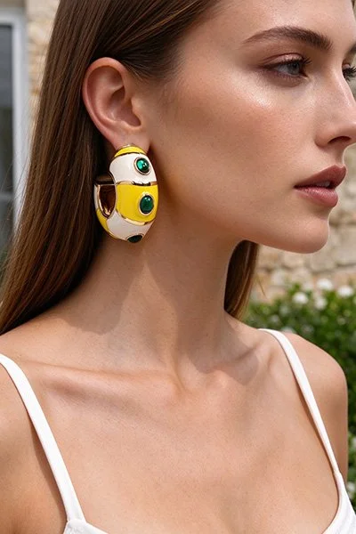 A woman wearing large, colorful earrings featuring a yellow, white, and green design with eye motifs.