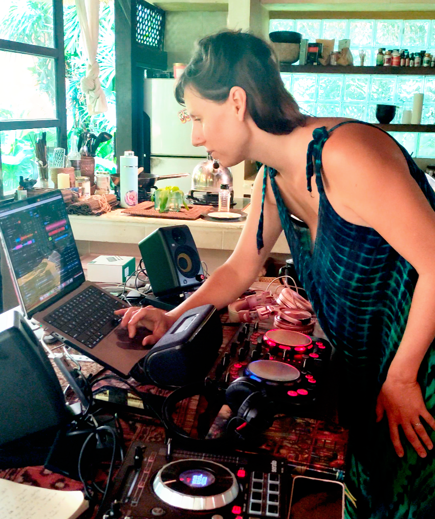 A woman with short dark hair using a laptop and DJ equipment on a kitchen counter.