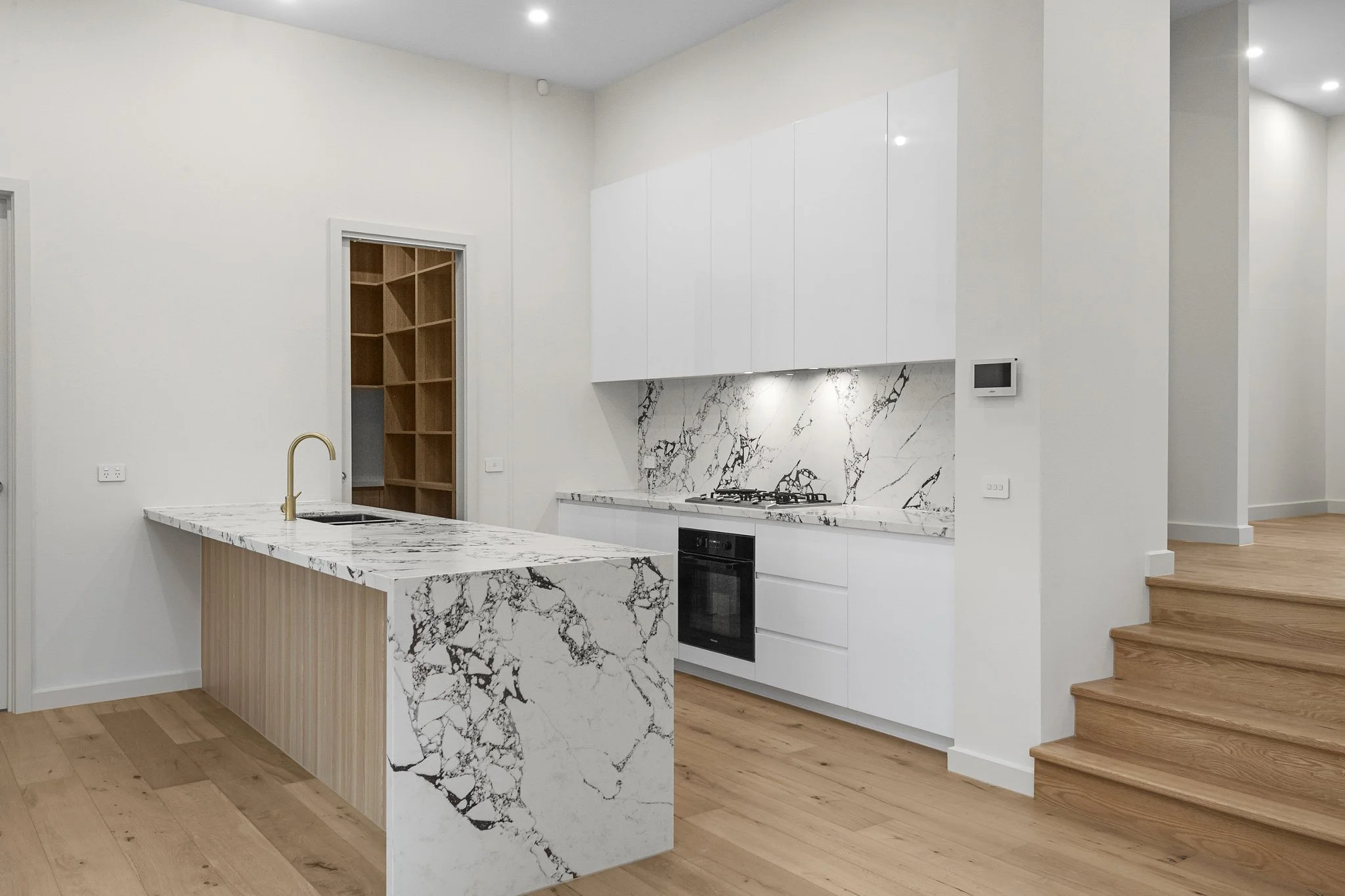 Modern kitchen with white cabinets, marble countertops, and a wooden staircase.