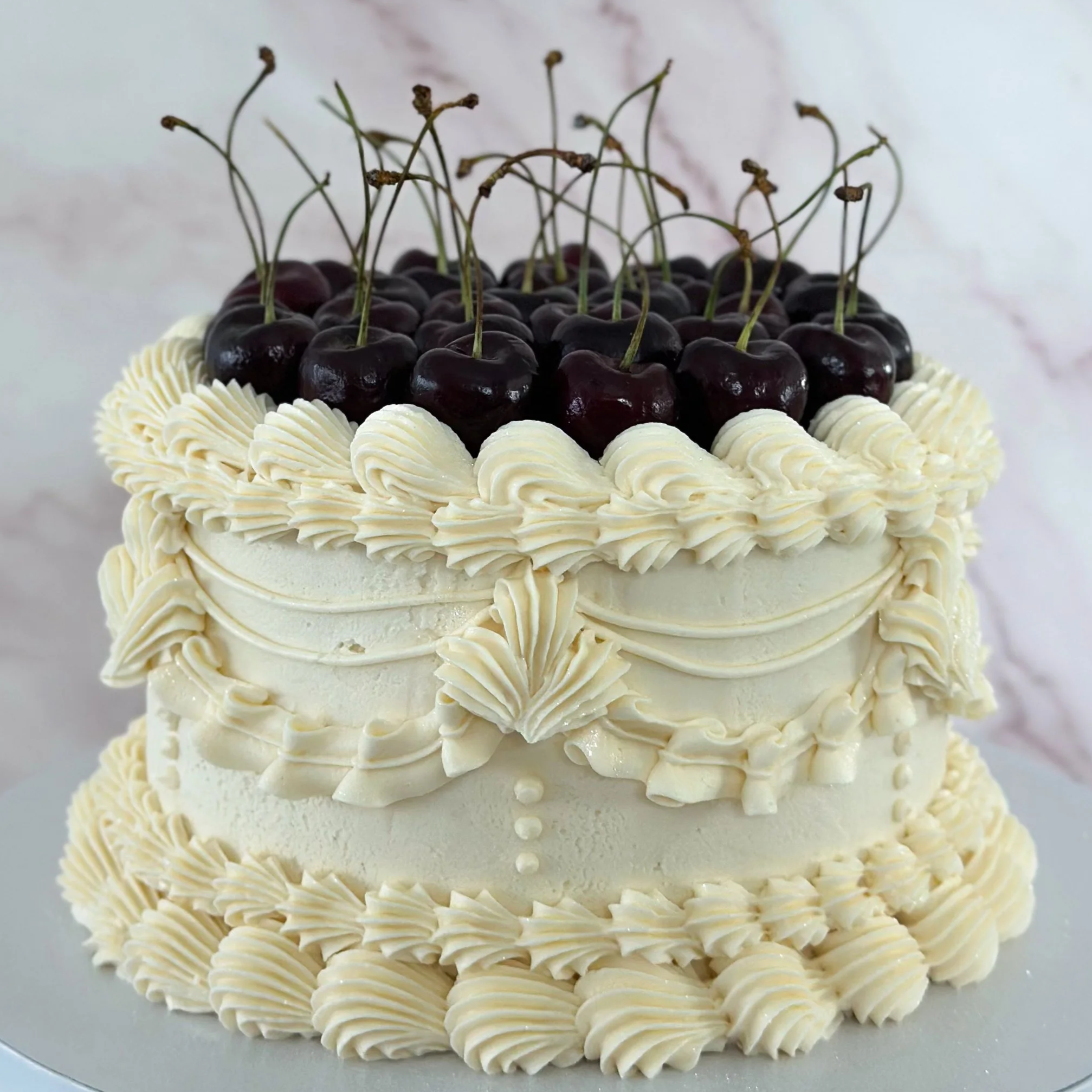 A round birthday cake decorated with pink, orange, and green buttercream flowers on a yellow fondant base, with pink buttercream rosette borders on top and bottom.