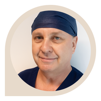 Portrait of a man wearing a navy surgical cap and scrubs, smiling softly.