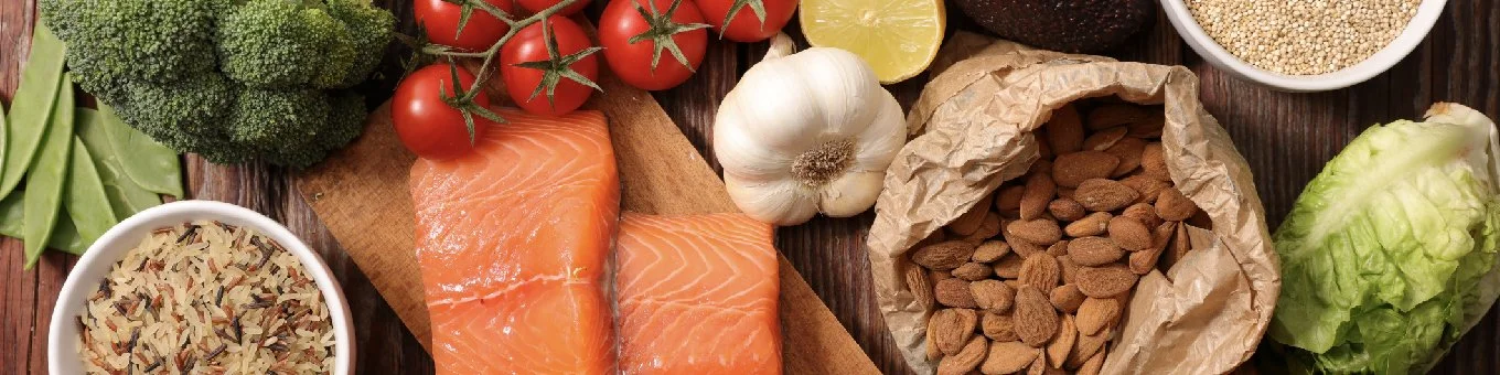 Fresh vegetables, salmon, garlic, almonds, rice, and lemon on a wooden surface.