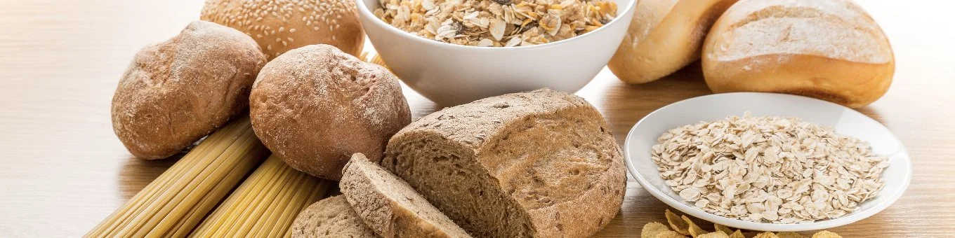 Assorted bread, oatmeal, and pasta on a wooden surface.