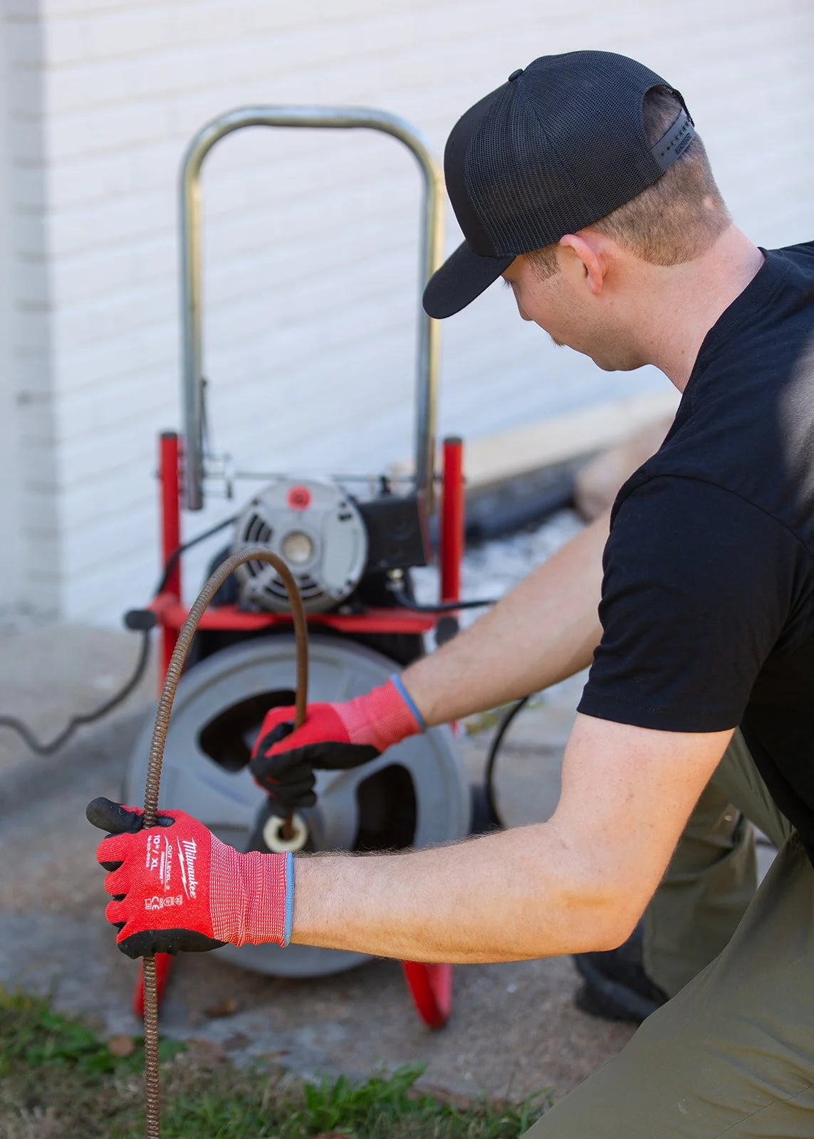 A modern house with wooden and stone exterior walls sits on a green hillside. In the background, there are snow-capped mountains under cloudy skies.