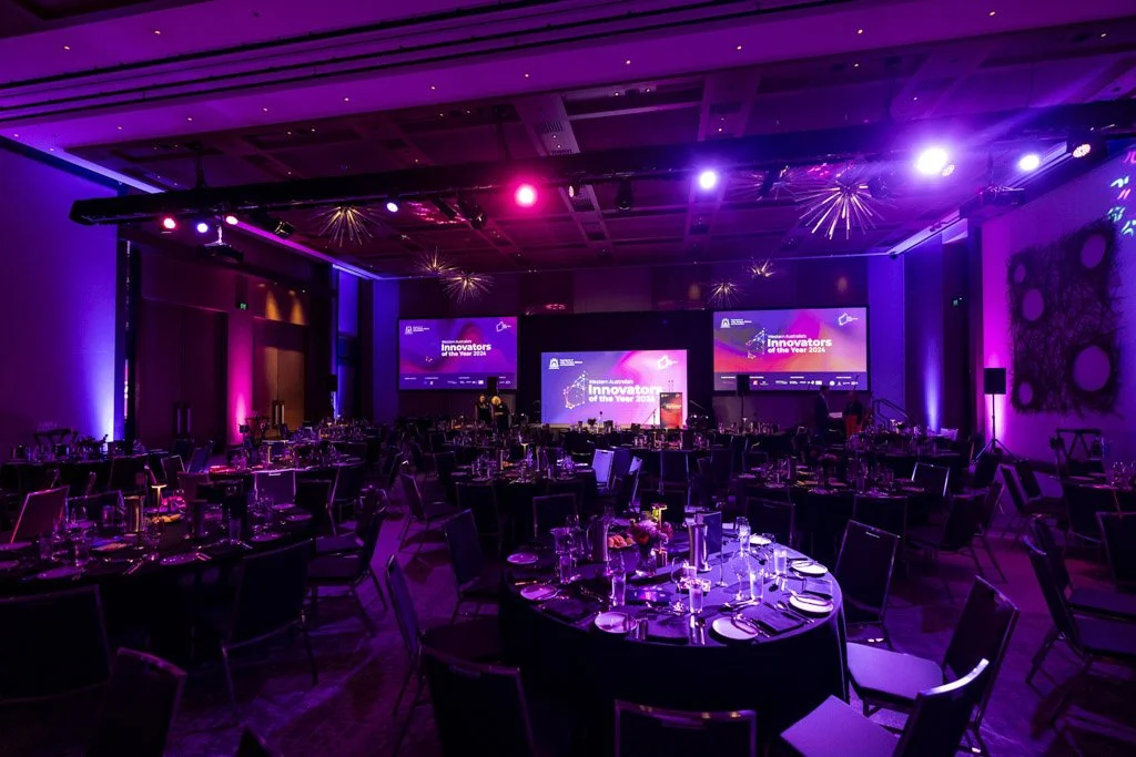 Ballroom set for Western Australia Innovator of the Year Awards 2024 with purple lighting and branded screens, styled by Event & Conference Co.