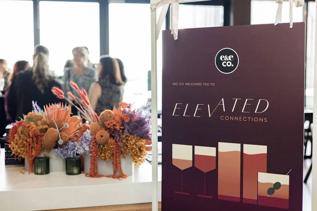 Sign reading ‘E&C Co. welcomes you to Elevated Connections’ beside colourful floral arrangements at a networking event in Perth.