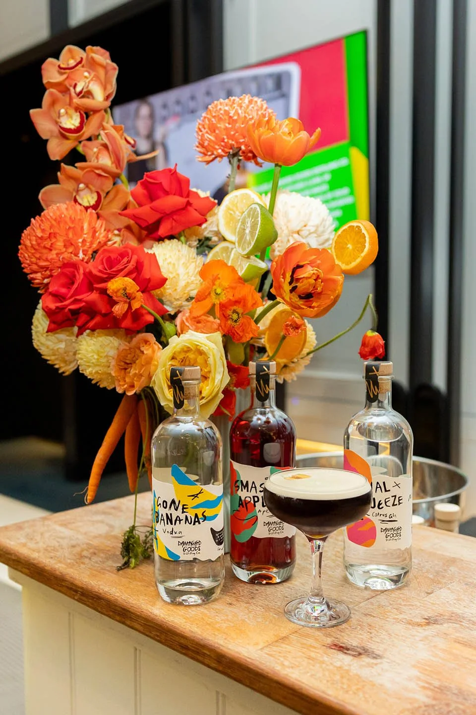 Bright orange and yellow floral display with Damaged Goods spirits bottles at the zero-waste cocktail bar for WasteSorted Awards Perth.