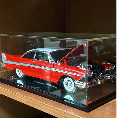 Red and white scale model vintage car with open hood inside glass display case.