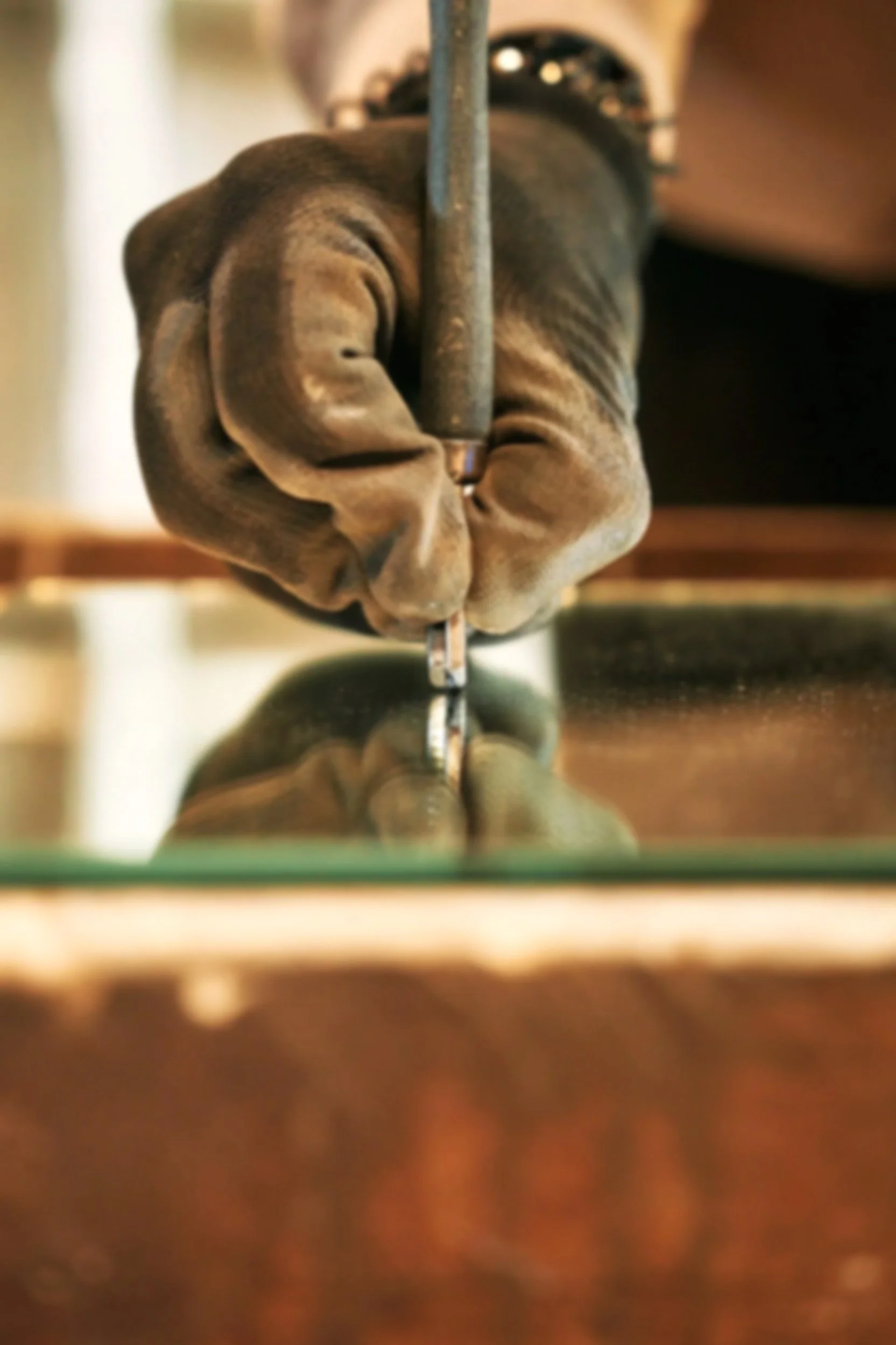 Close-up of a person's hand in a glove, using a wrench to tighten a bolt on a glass surface, with their reflection visible.