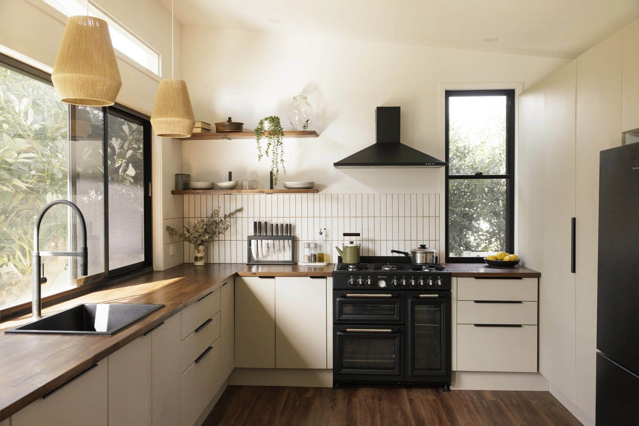 Modern kitchen with wood countertops, black stove, white cabinets, black fridge, large window, and pendant lights