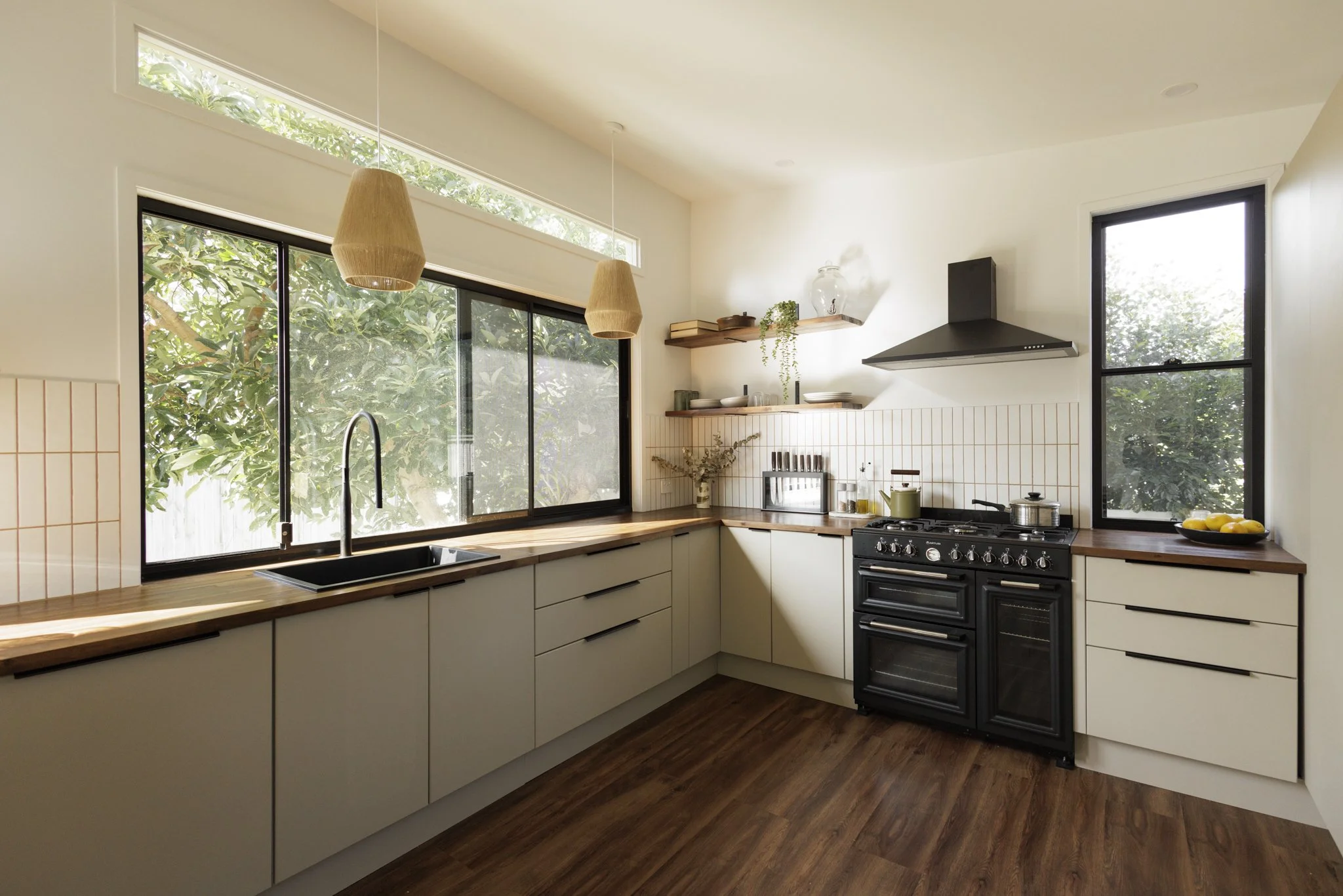 Modern kitchen with white cabinets, wooden countertops, black stove, and large windows bringing in natural light.