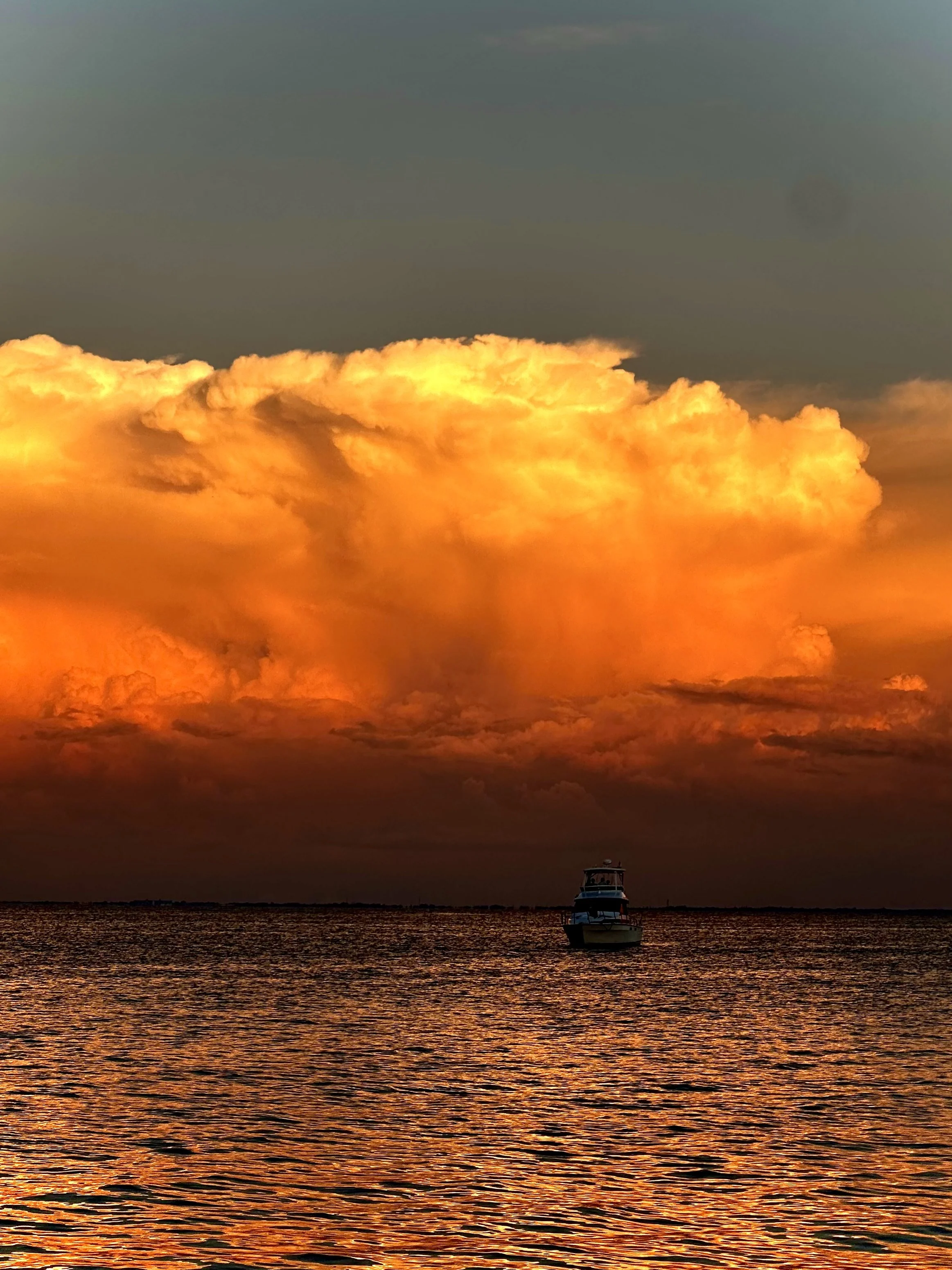 A boat floating on calm waters under a vibrant orange and yellow sunset sky with scattered clouds.