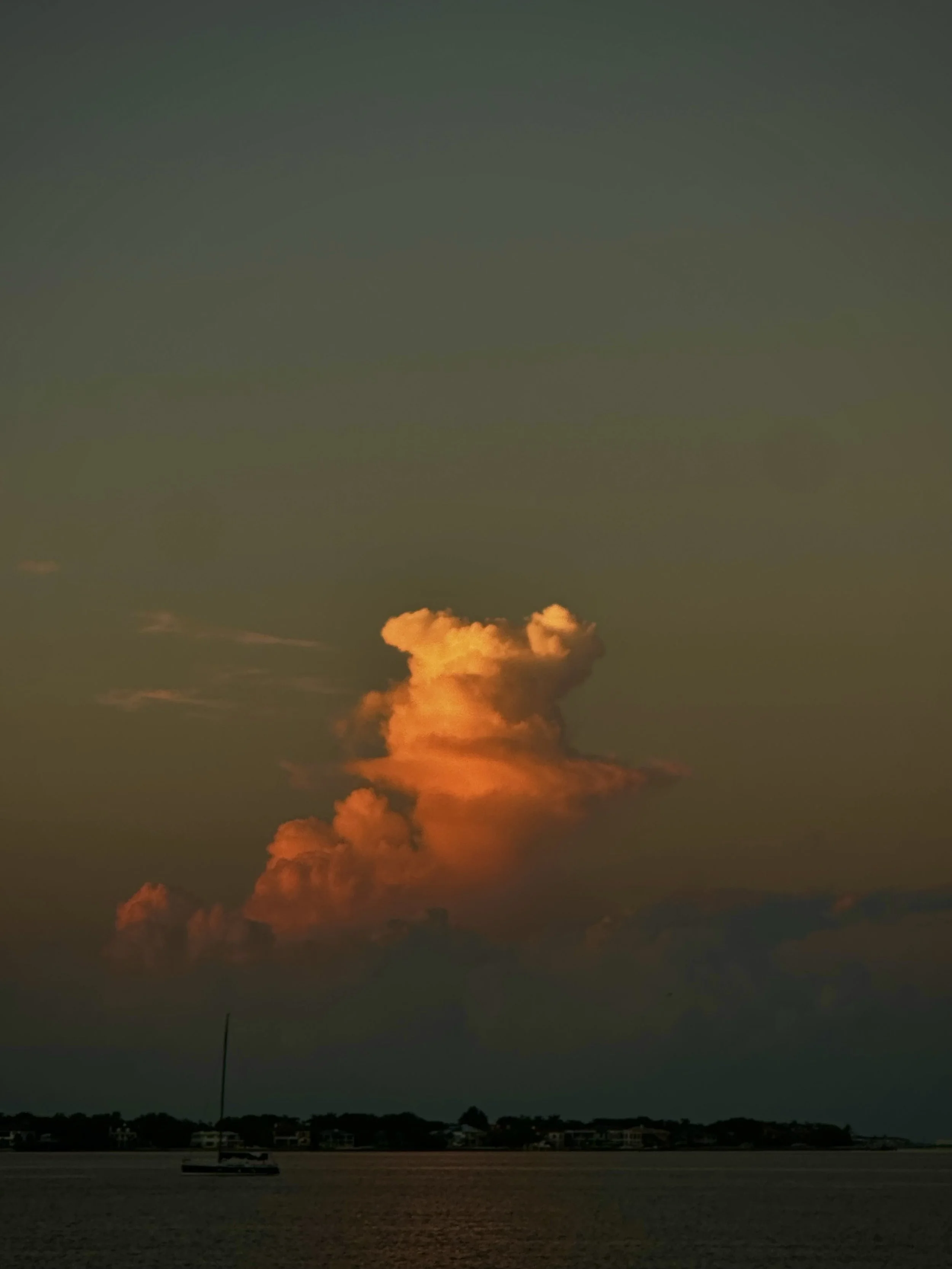 Sunset over water with orange and yellow clouds in the sky, and a small sailboat in the foreground.