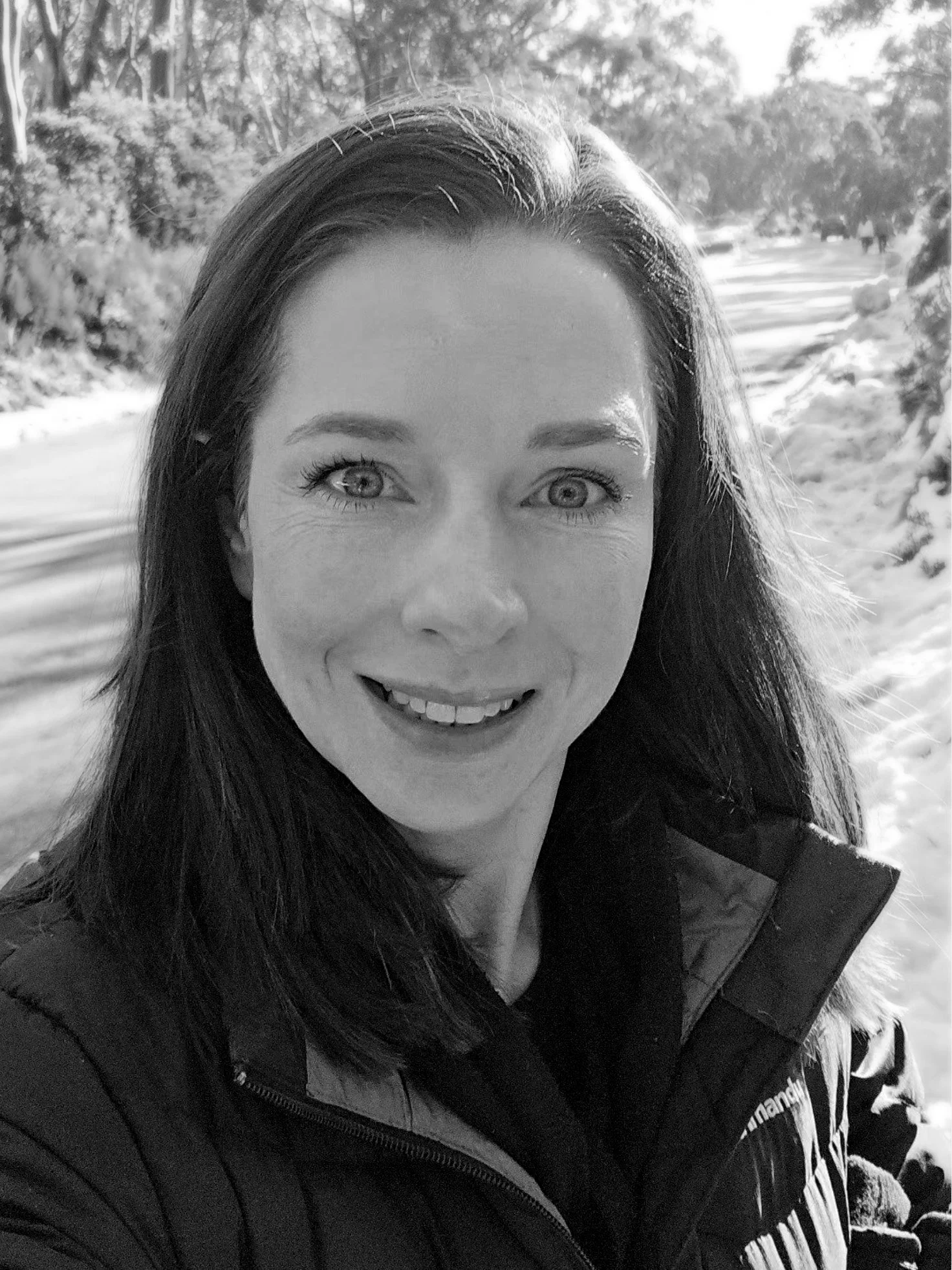 A woman with long dark hair taking a selfie outdoors in a snowy landscape, wearing a winter jacket.