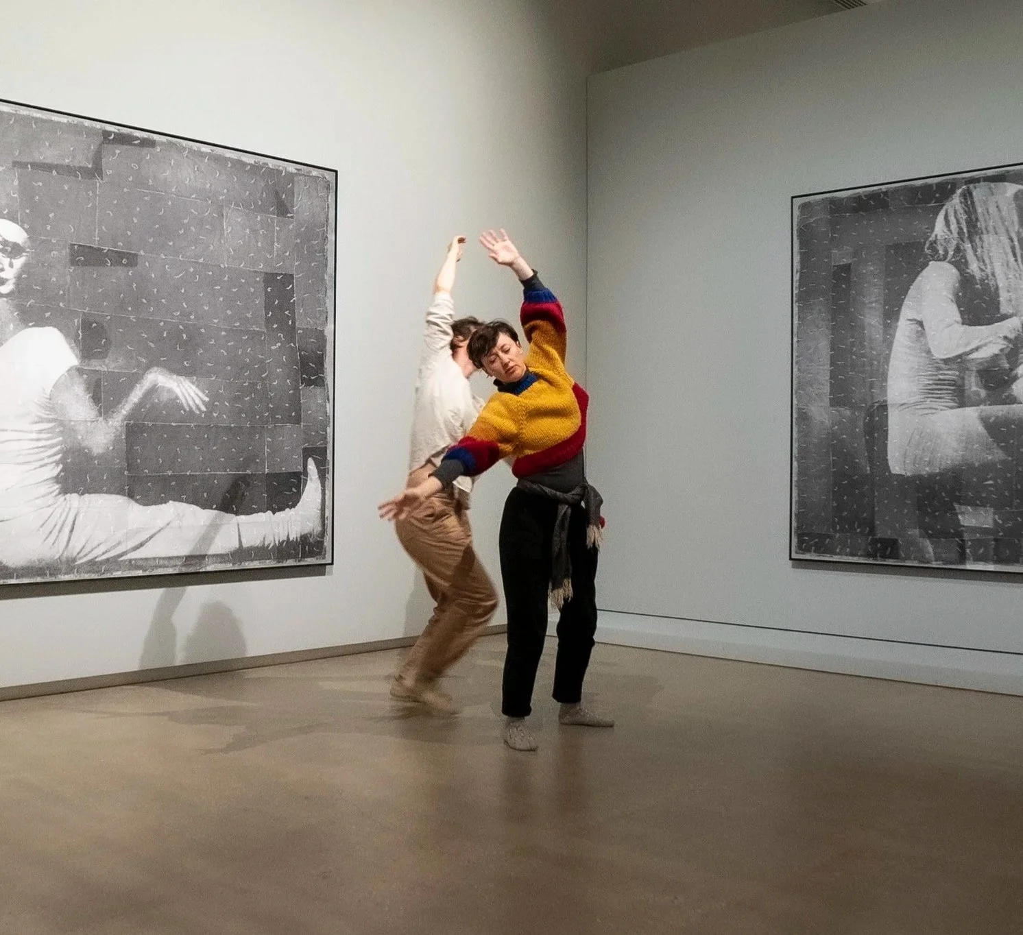 Two people dancing in an art gallery, surrounded by large black and white photographs on the wall.