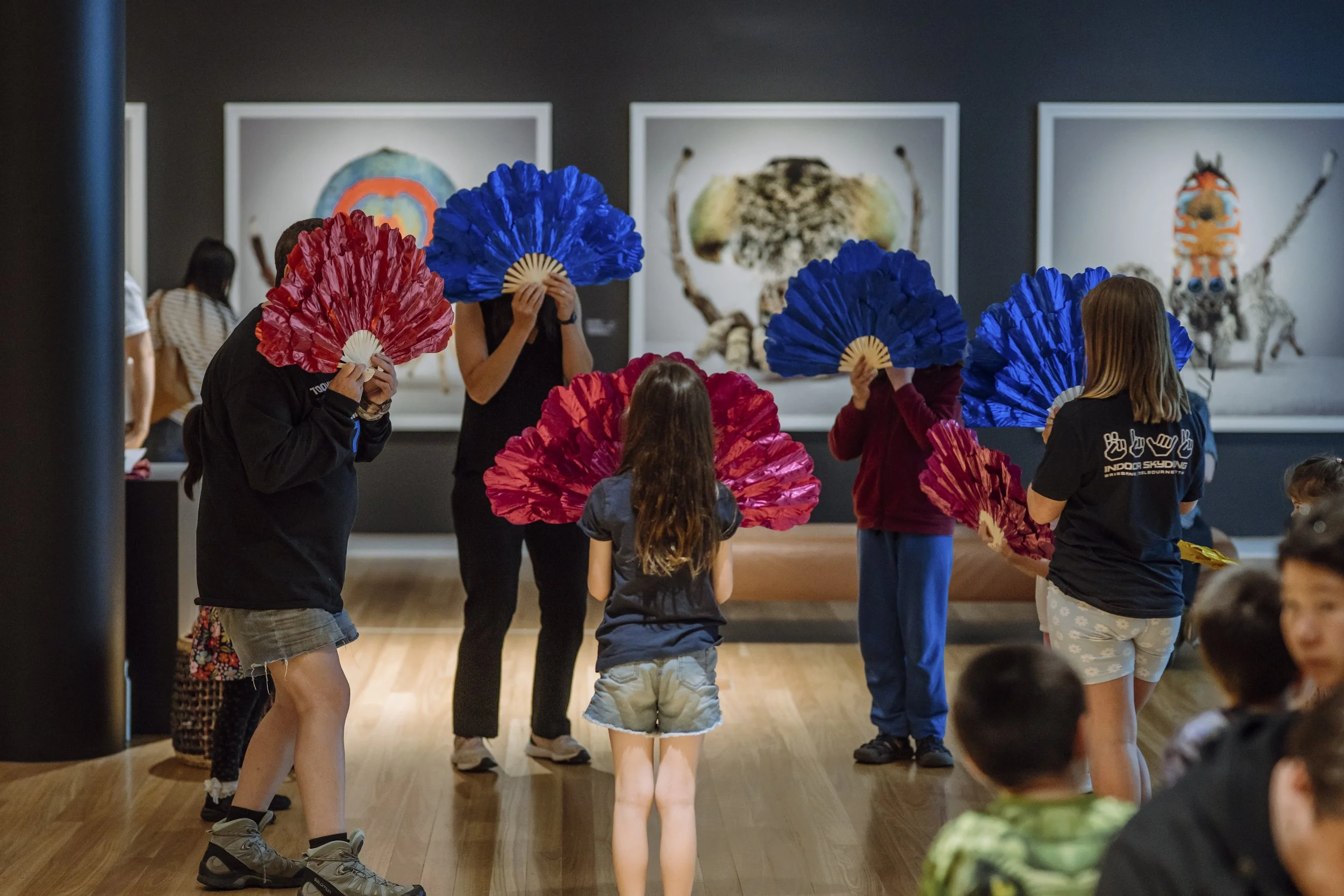 People holding red and blue fans in an art gallery, viewing artwork on the wall.