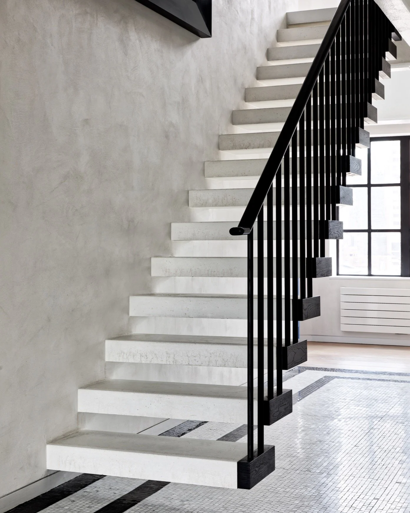 Modern staircase with white steps and a black railing in an interior space with large windows.