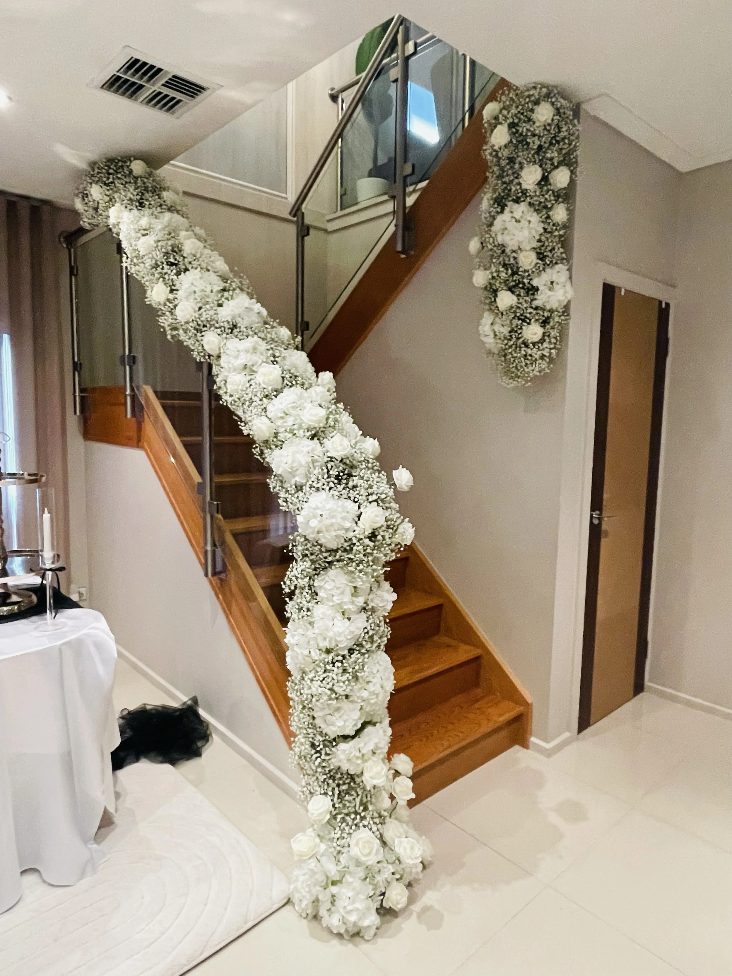 A staircase decorated with a cascading floral arrangement of white flowers, including roses and baby's breath, at an indoor event or celebration.