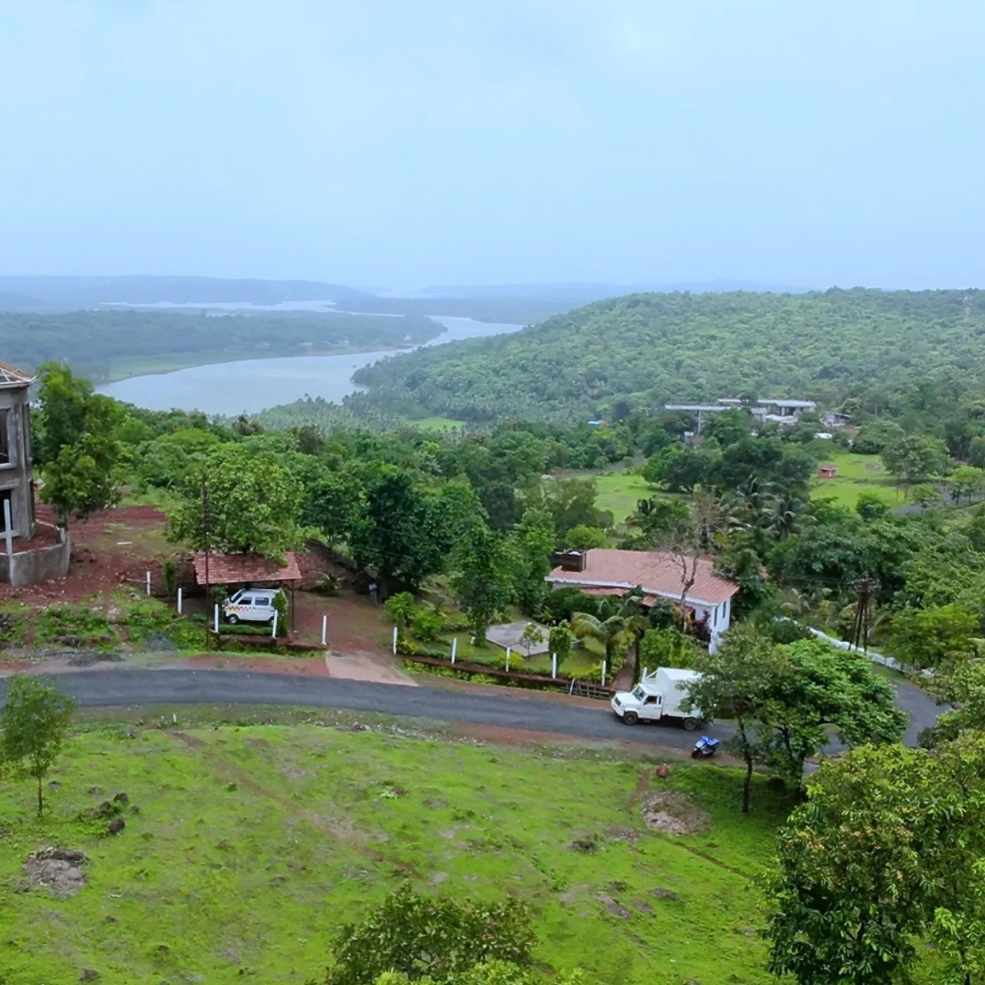 A scenic view of a hilly landscape with lush green trees, a river meandering through the valley, and houses scattered across the hillside, under a cloudy sky. - Kinale Plot For Sale