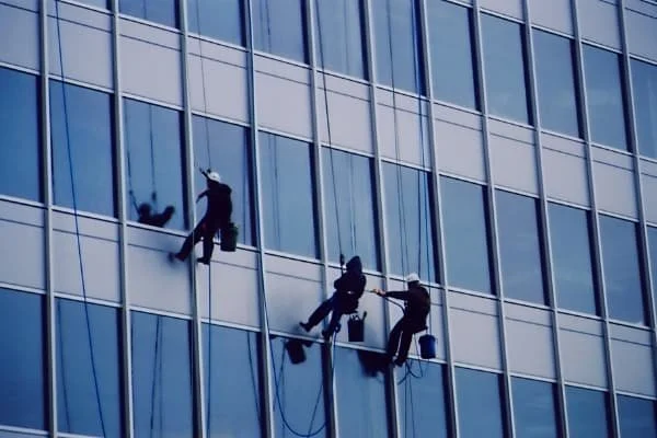 Three window washers cleaning the windows of a tall office building.