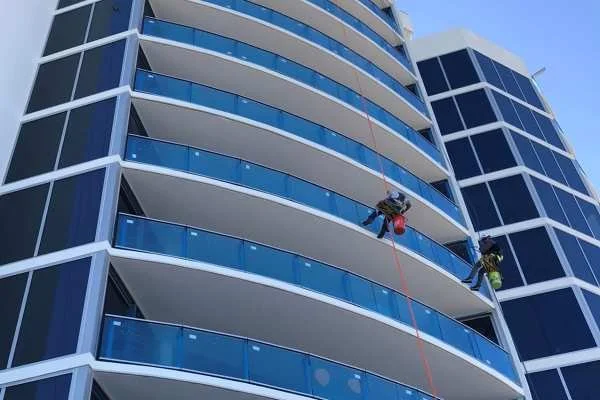 Workers cleaning the windows of a modern high-rise apartment building from a suspended platform.