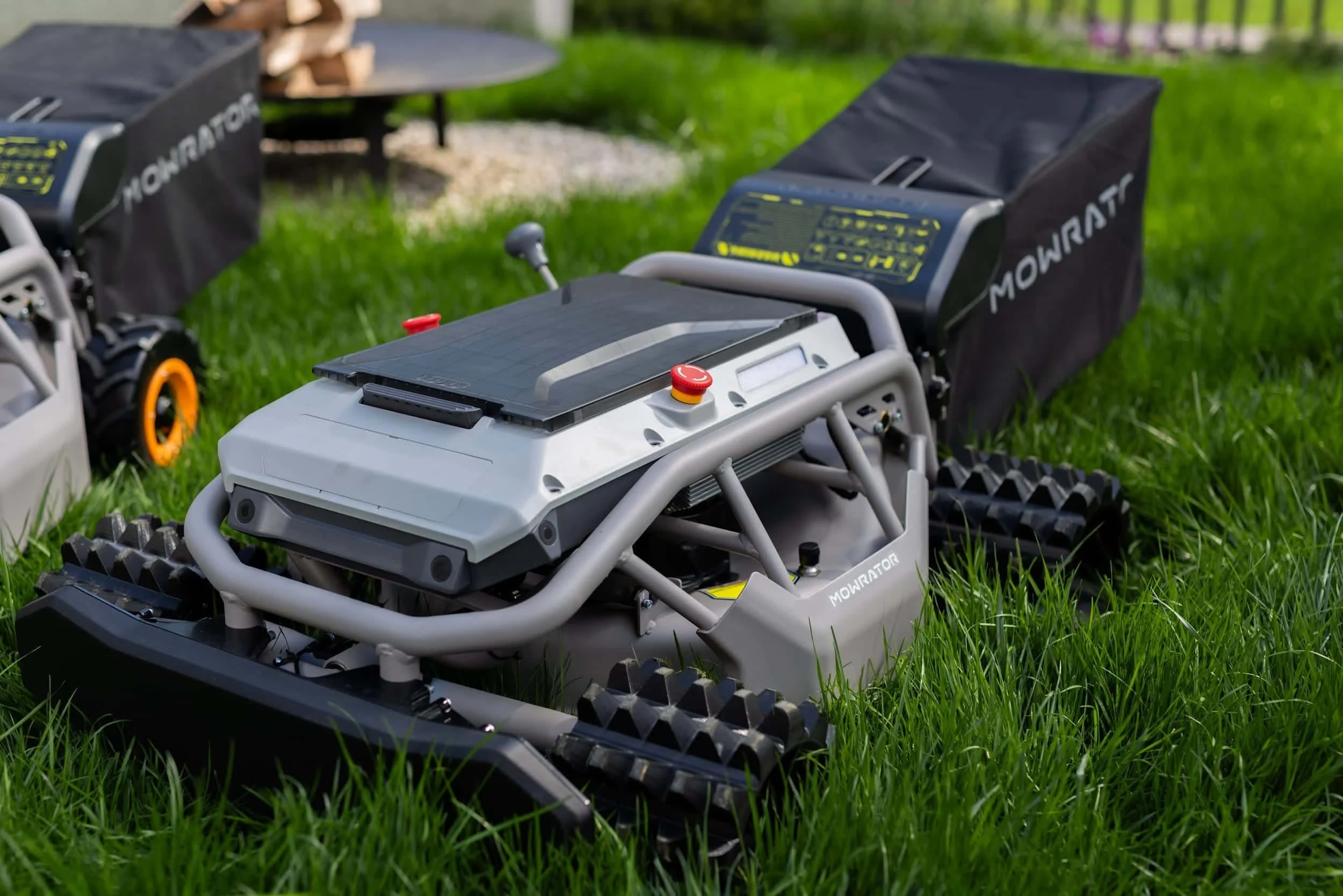 A robotic lawn mower on grass with a control panel, tracks, and various mechanical parts.