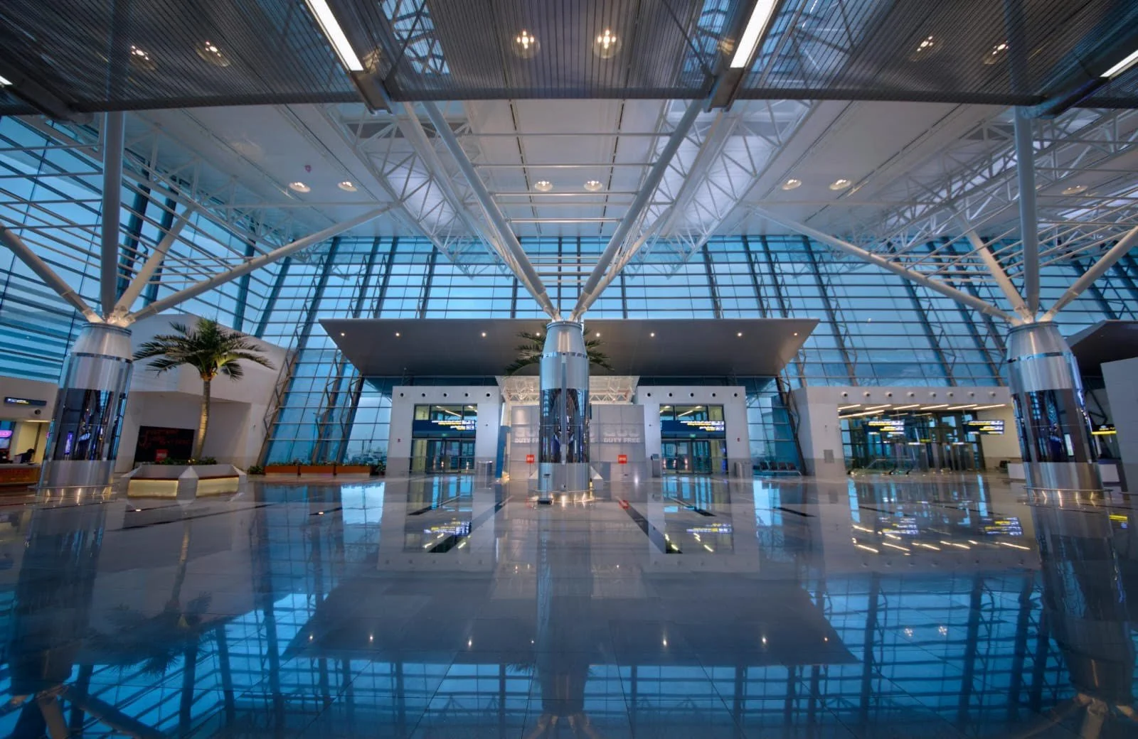 Empty modern airport terminal with a high glass ceiling, metal support beams, and polished reflective floors.