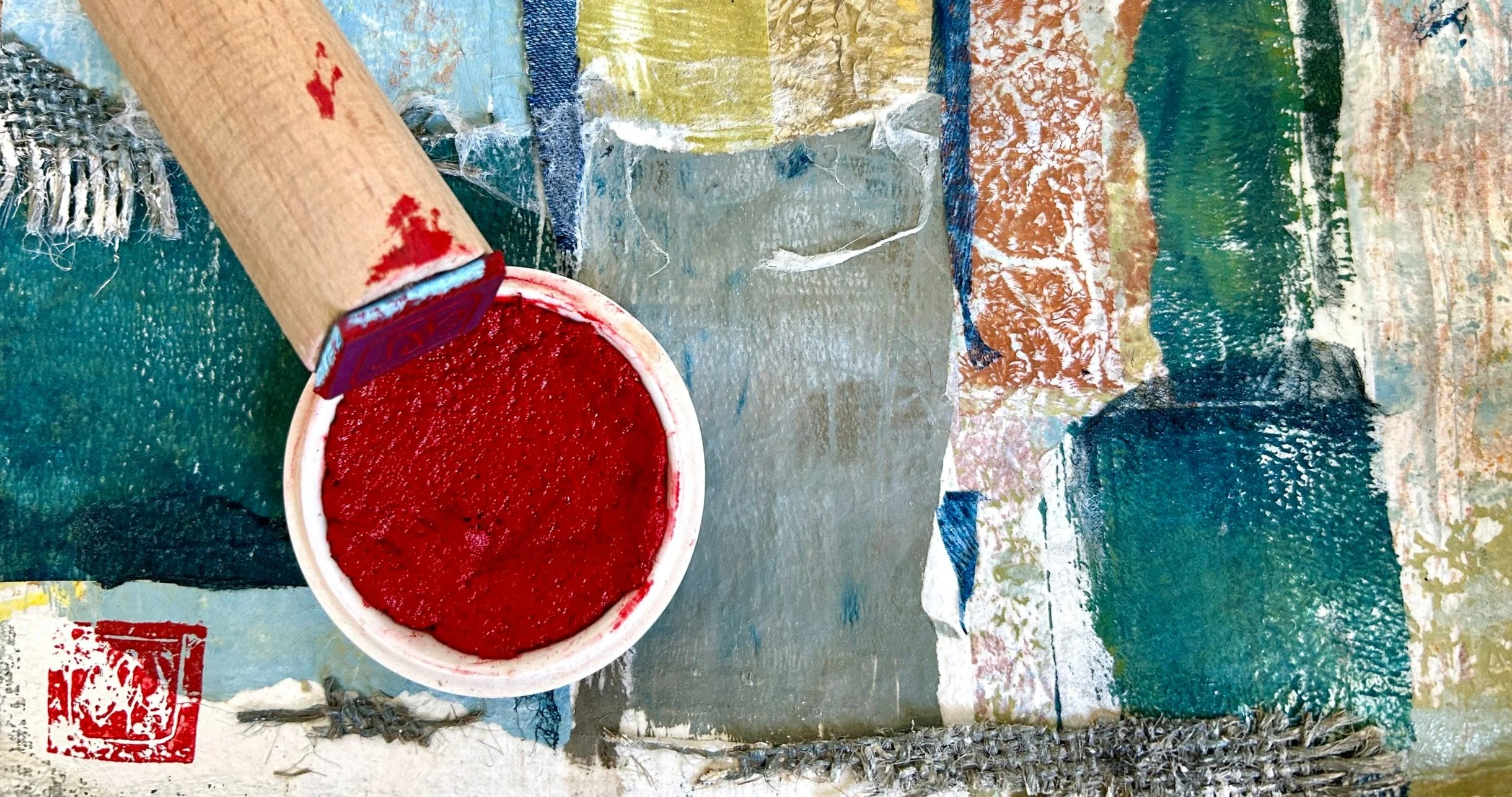 An open container of bright red paint on a colorful, textured surface with various painted patches and markings.