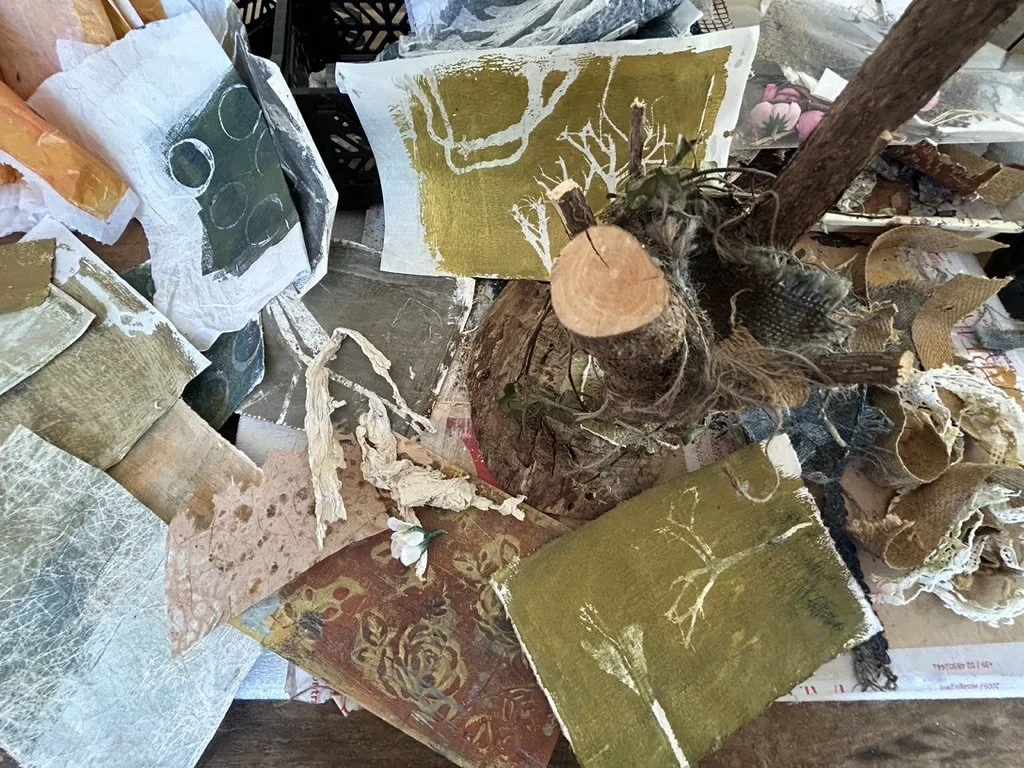 Gepresste Blumen, umgeben von verschiedenen Kunstwerken und Papierarbeiten auf einem Tisch.