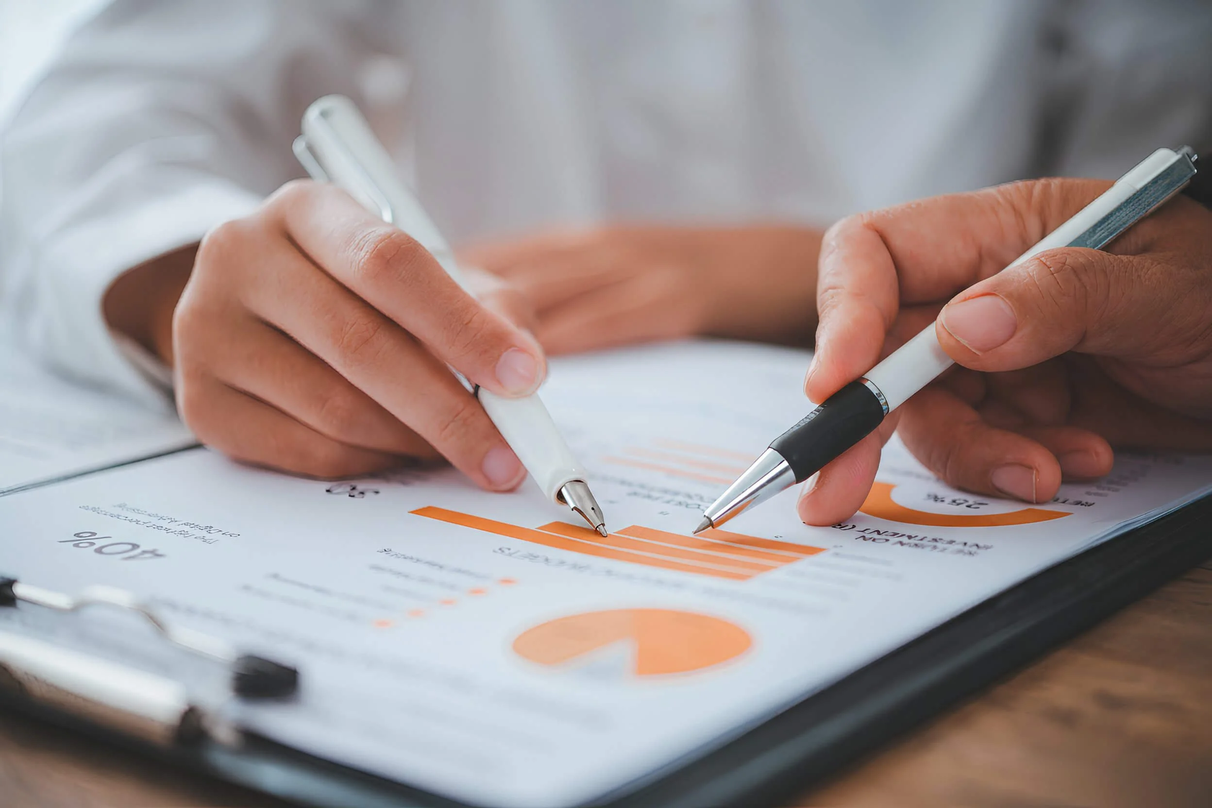 Close-up of hands signing a document with pens, placed on a clipboard.