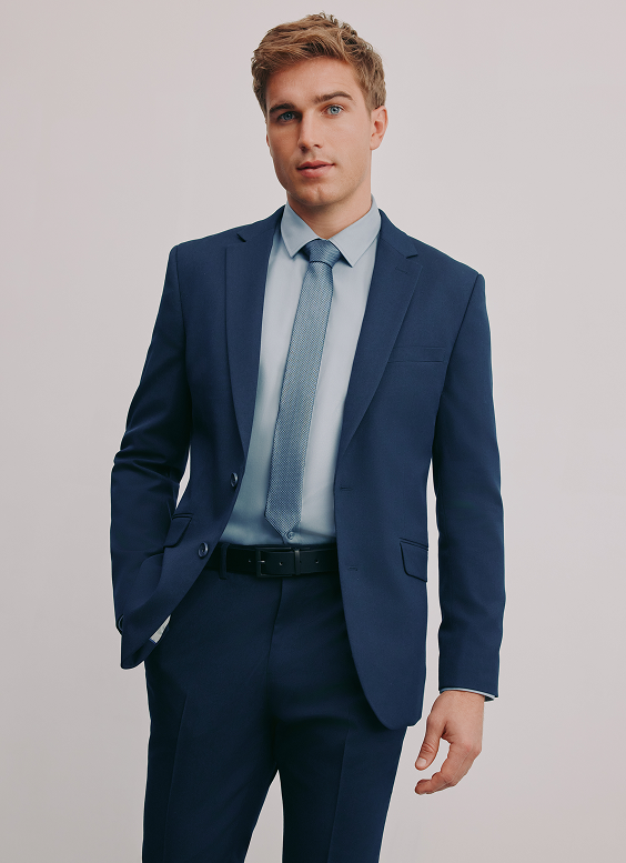 Young man in a navy blue suit with a light blue shirt and patterned tie, posing against a plain light background.