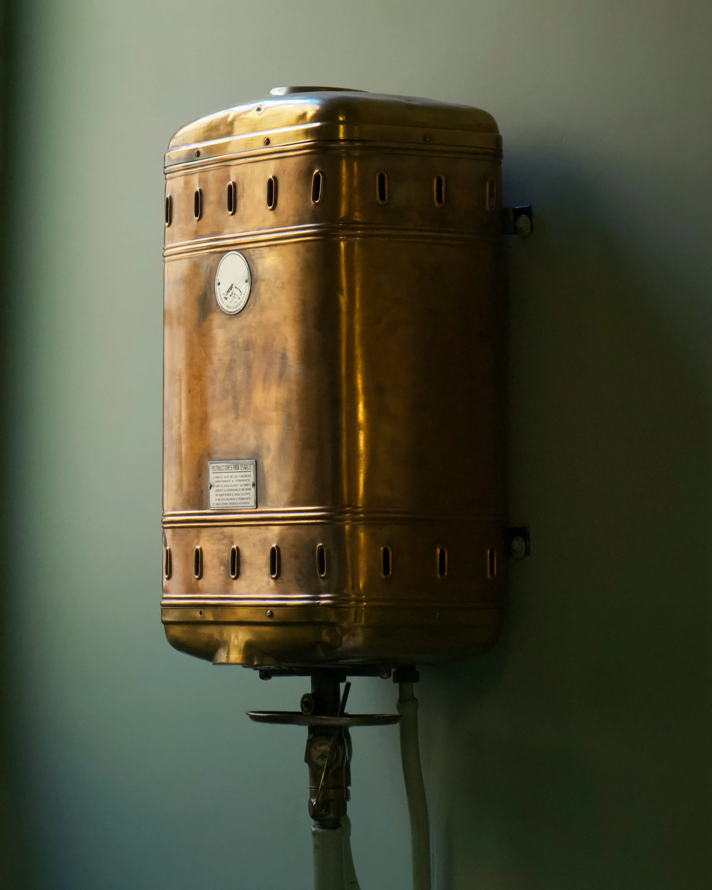 Brass automatic hand dryer mounted on a wall with electrical cords.
