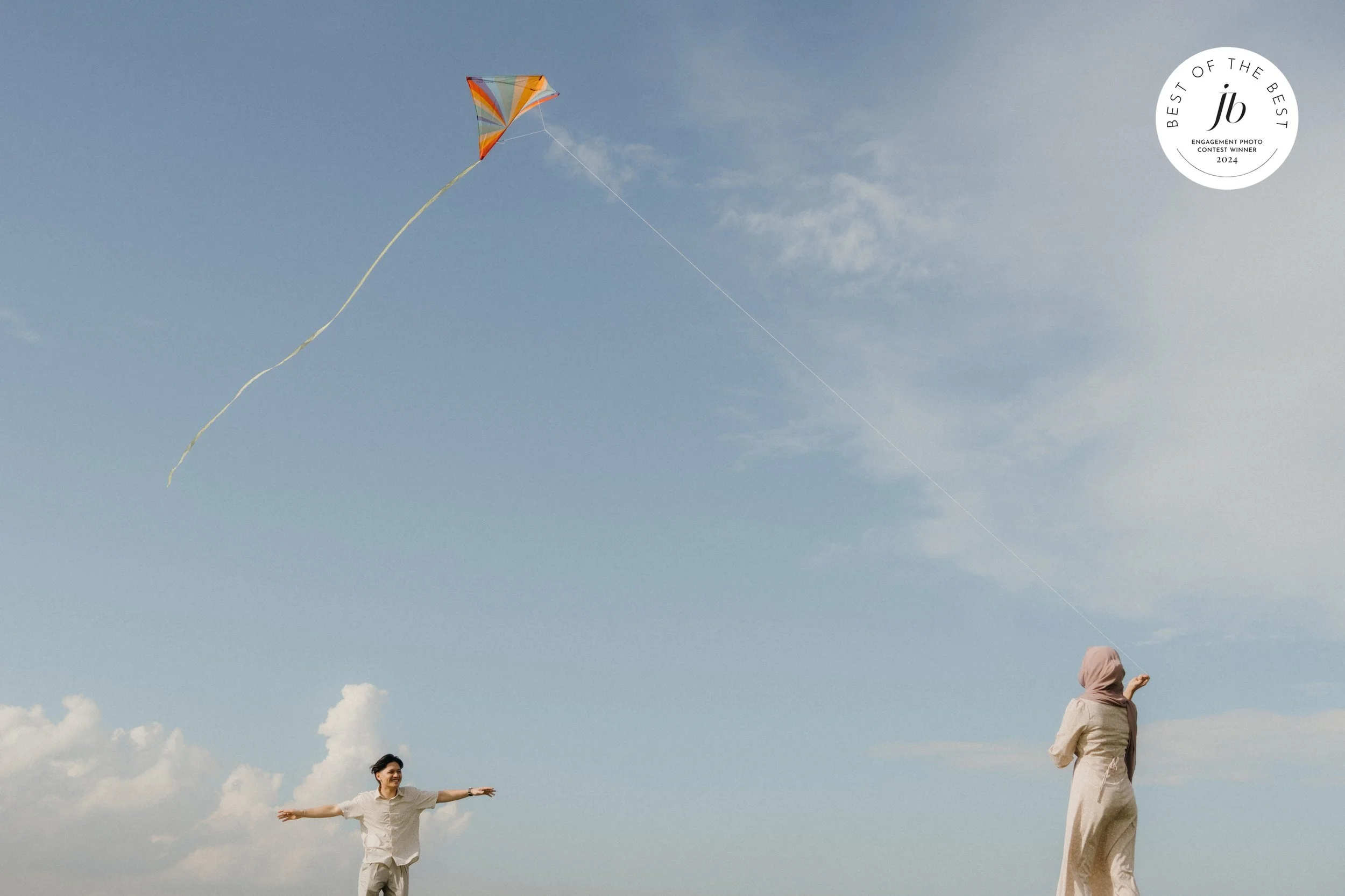 Two women flying a colorful kite in the sky on a clear day, with one woman holding the string and the other standing with arms outstretched.