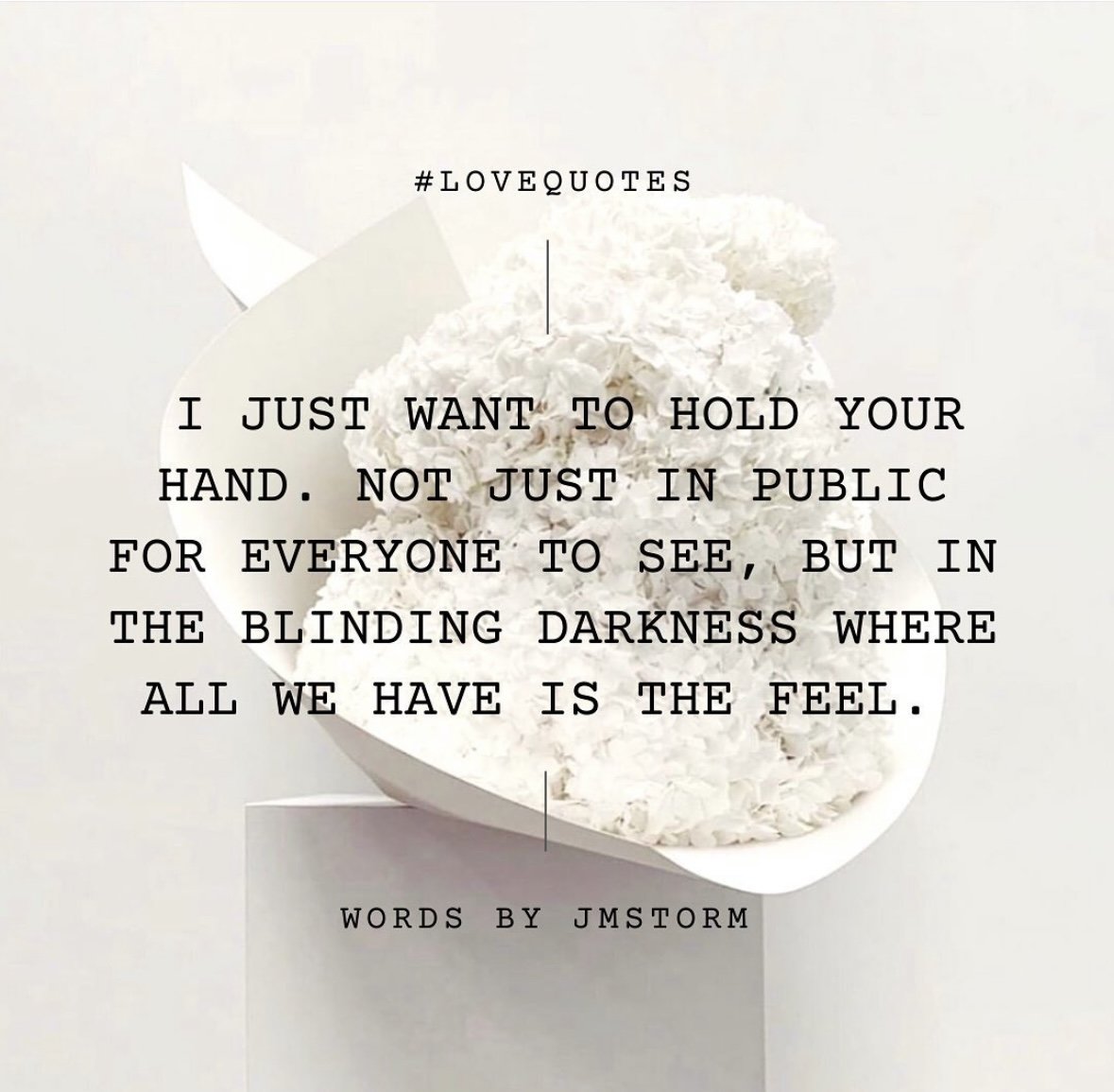 A quote over a background of white flowers and a white bowl. The quote reads: '#LOVEQUOTES I just want to hold your hand. Not just in public for everyone to see, but in the blinding darkness where all we have is the feel. Words by JMSTORM.'