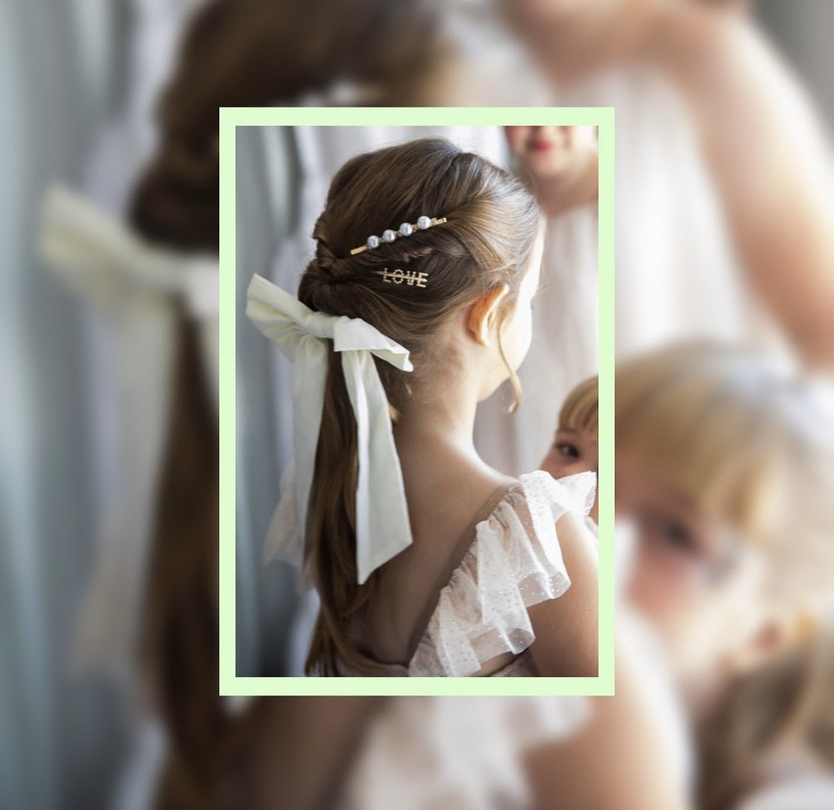 Close-up of a young girl with brown hair styled in a braid, adorned with a decorative hairpin that spells out 'LOVE' and a pearl headband, wearing a white dress with ruffled sleeves, at a formal event