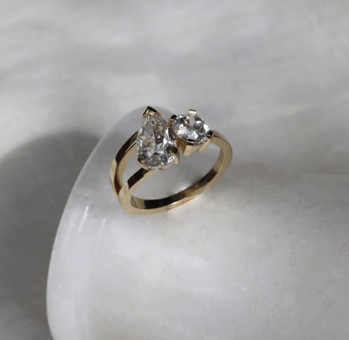 Gold ring with two large hearts-shaped and round-cut diamonds on a white surface.