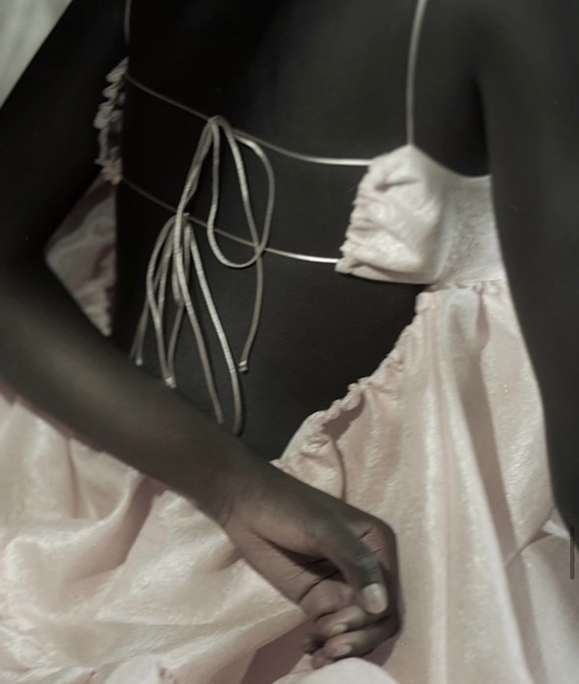 Close-up of a person wearing a black dress with satin ribbons and a pink satin skirt, with their hand resting on their waist.