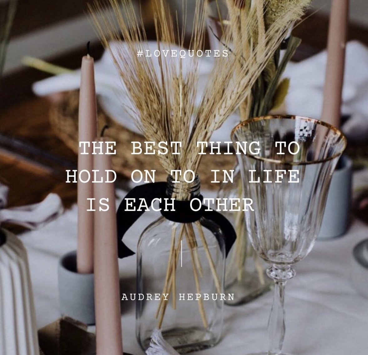 Decorative table setting with dried wheat in a glass jar, pink taper candles, and a wine glass, with an inspirational quote by Audrey Hepburn overlaid.