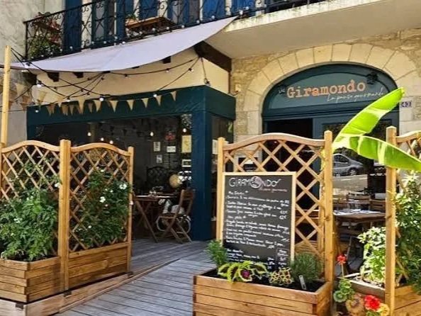 Outdoor dining area of a restaurant named 'Giramondo', with wooden fencing, potted plants, and a chalkboard menu, in an urban setting.
