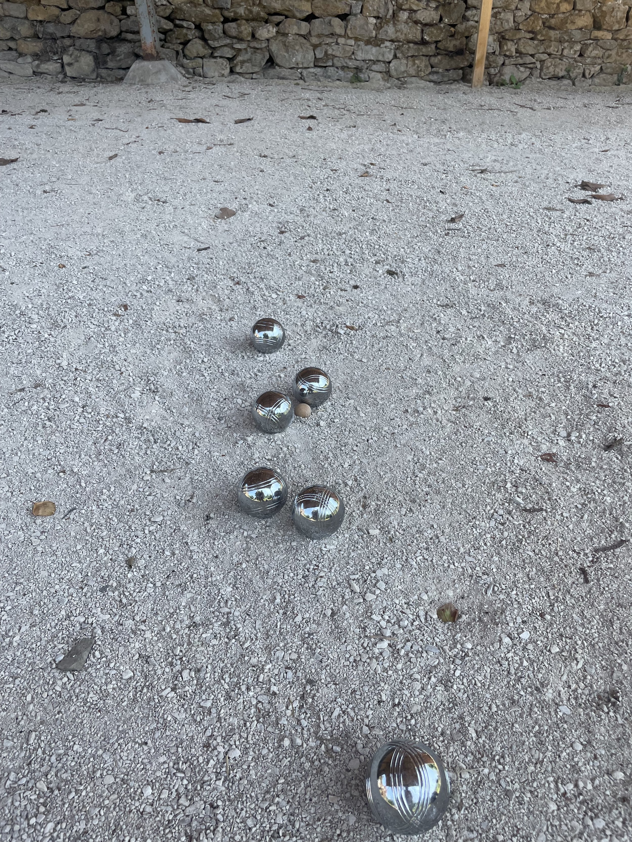 A gravel court with several metallic pétanque balls