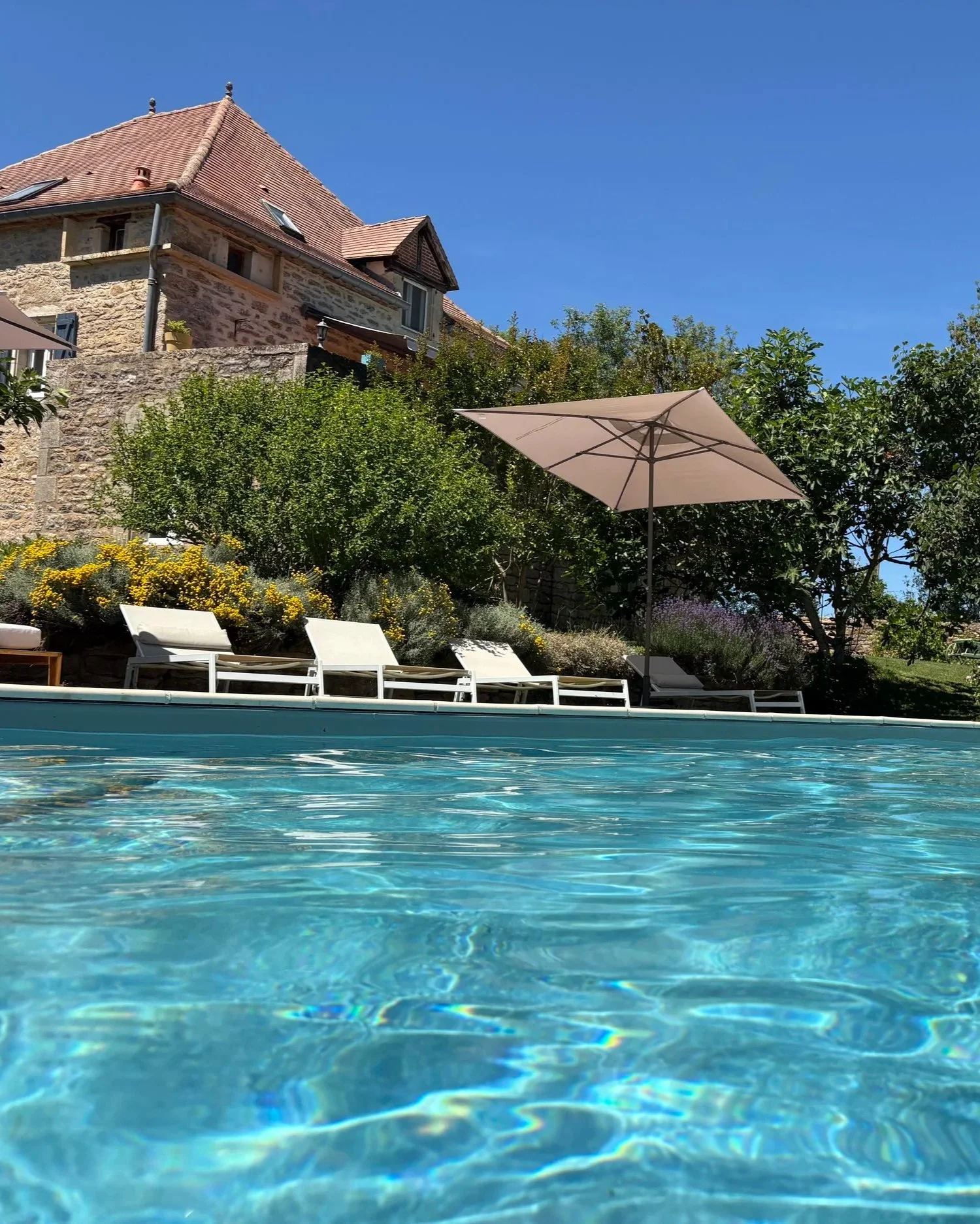 Une piscine entourée de transats et d'un grand parasol beige.