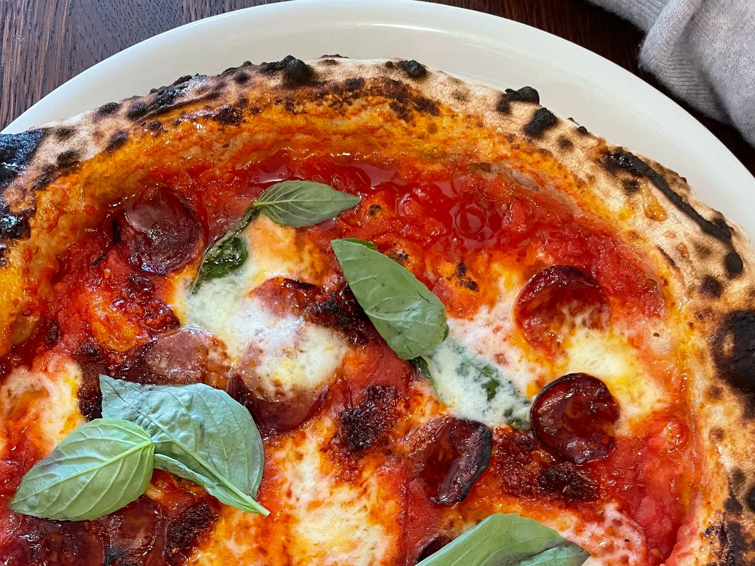 Close-up of a pizza with tomato sauce, melted cheese, pepperoni, and basil leaves on top.