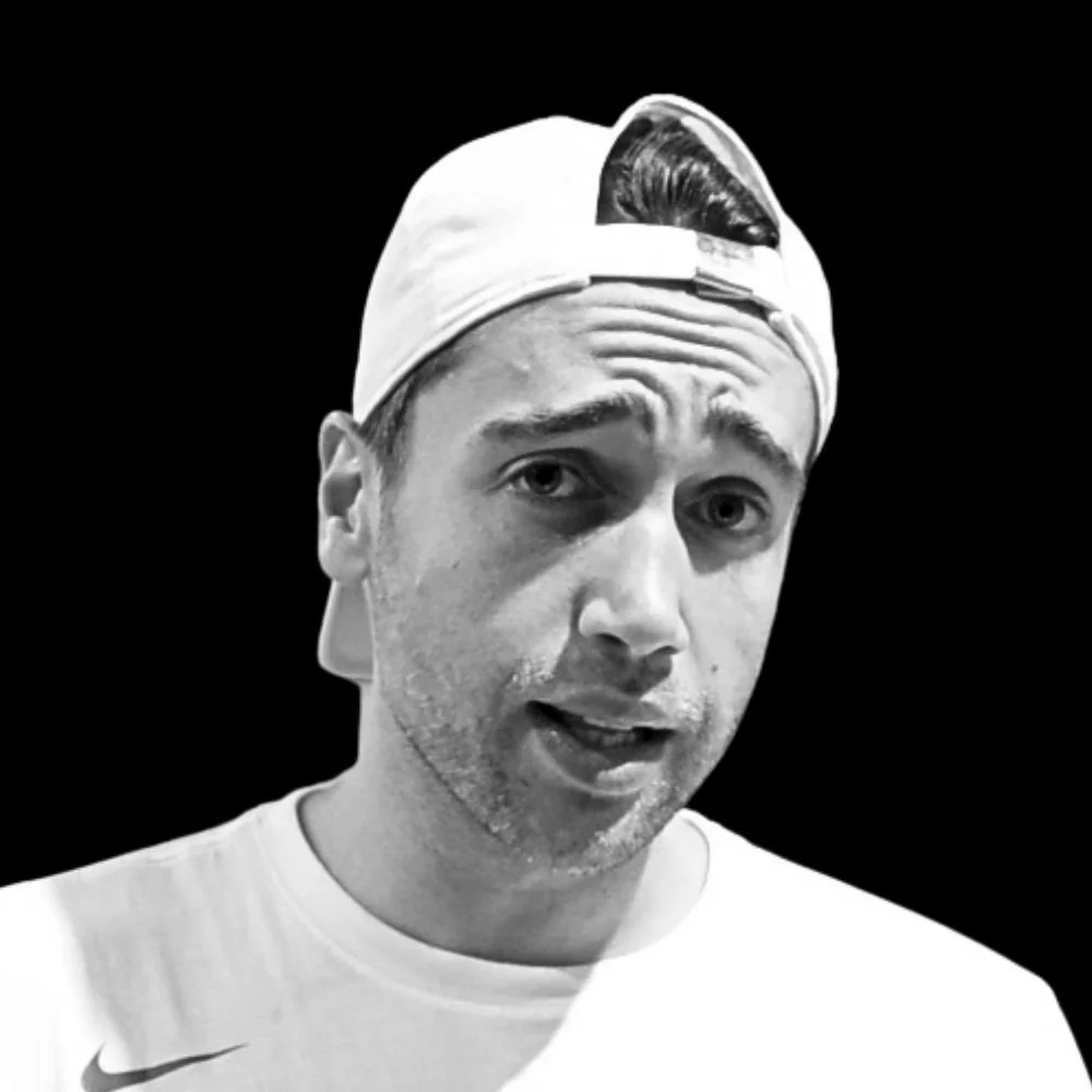 Black and white photo of a young man wearing a white cap backwards and a white sports shirt, with a serious expression, set against a black background.