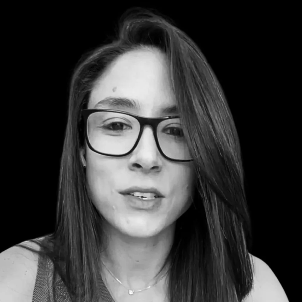 Black and white photo of a young woman with straight hair, wearing glasses, smiling slightly, against a black background.