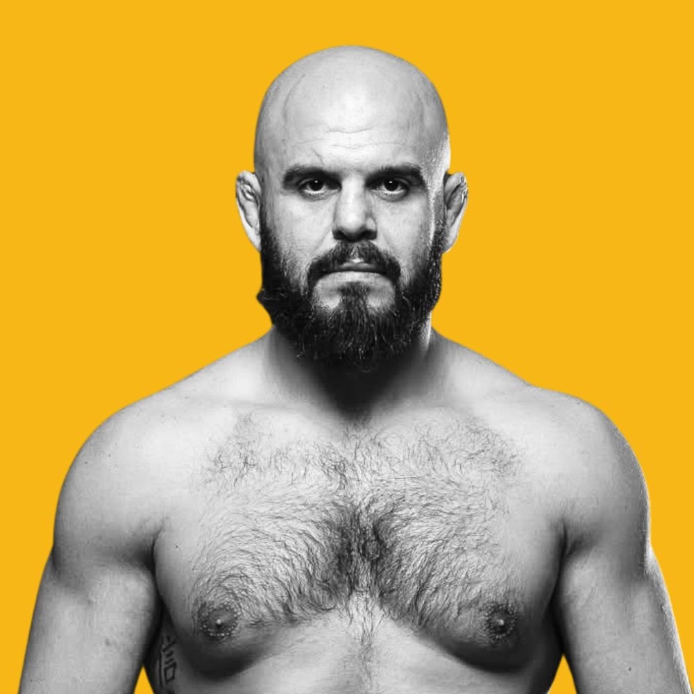 A black and white photo of a shirtless man with a beard and bald head against a yellow background.