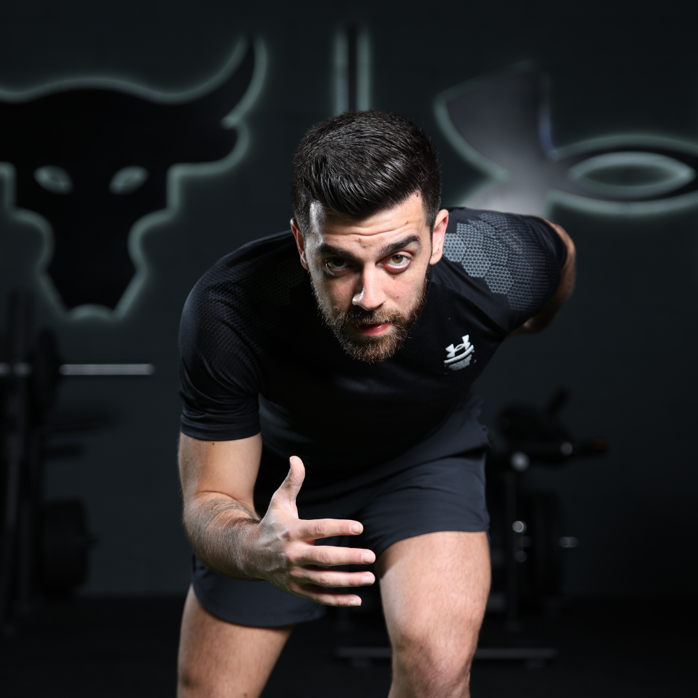 A young man in athletic wear is leaning forward in a running stance in a gym, preparing to sprint, with a serious expression on his face.