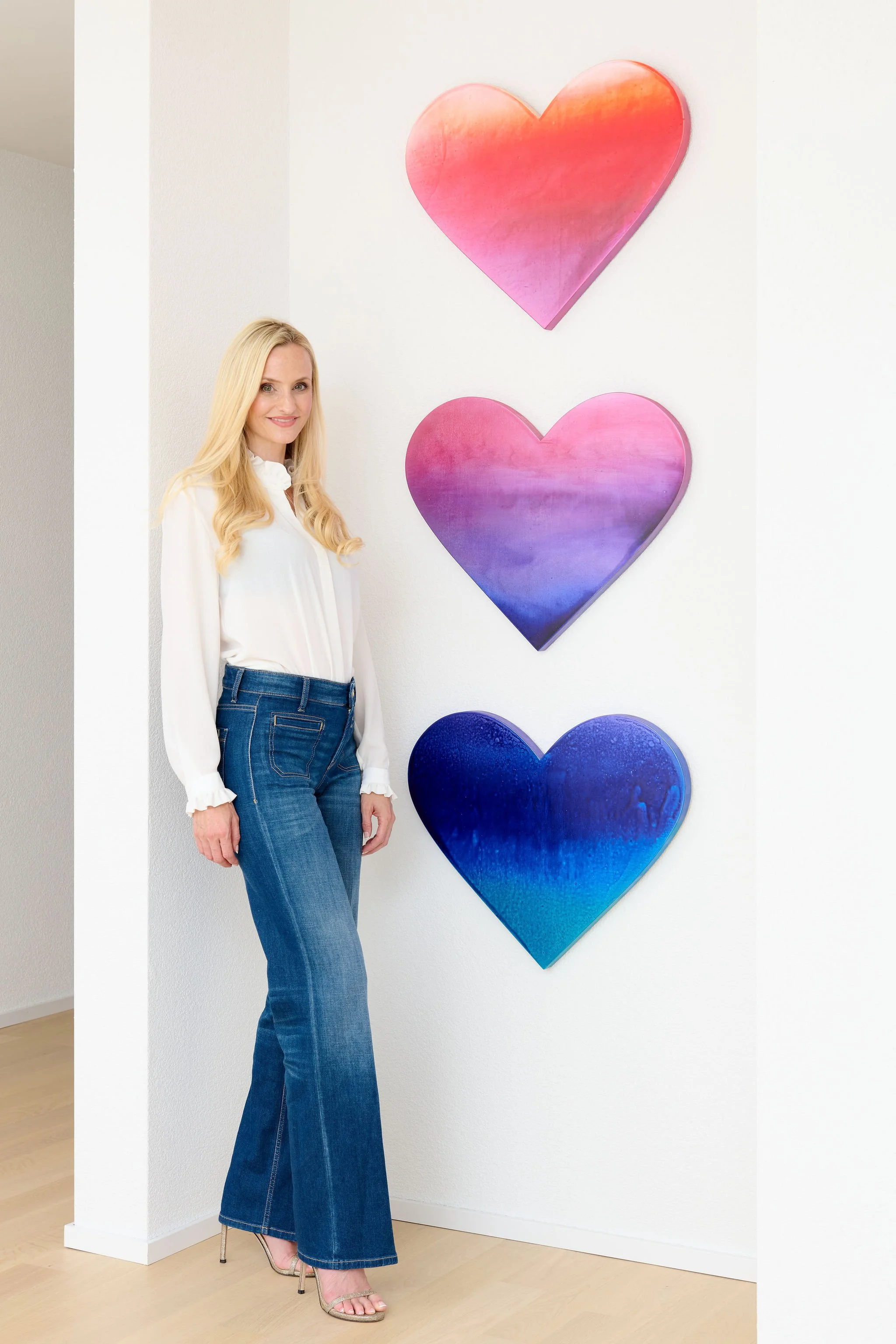 Valentina Blumer, Schweizer Künstlerin, im Atelier vor drei farbigen Herzkunstwerken an einer weissen Wand.