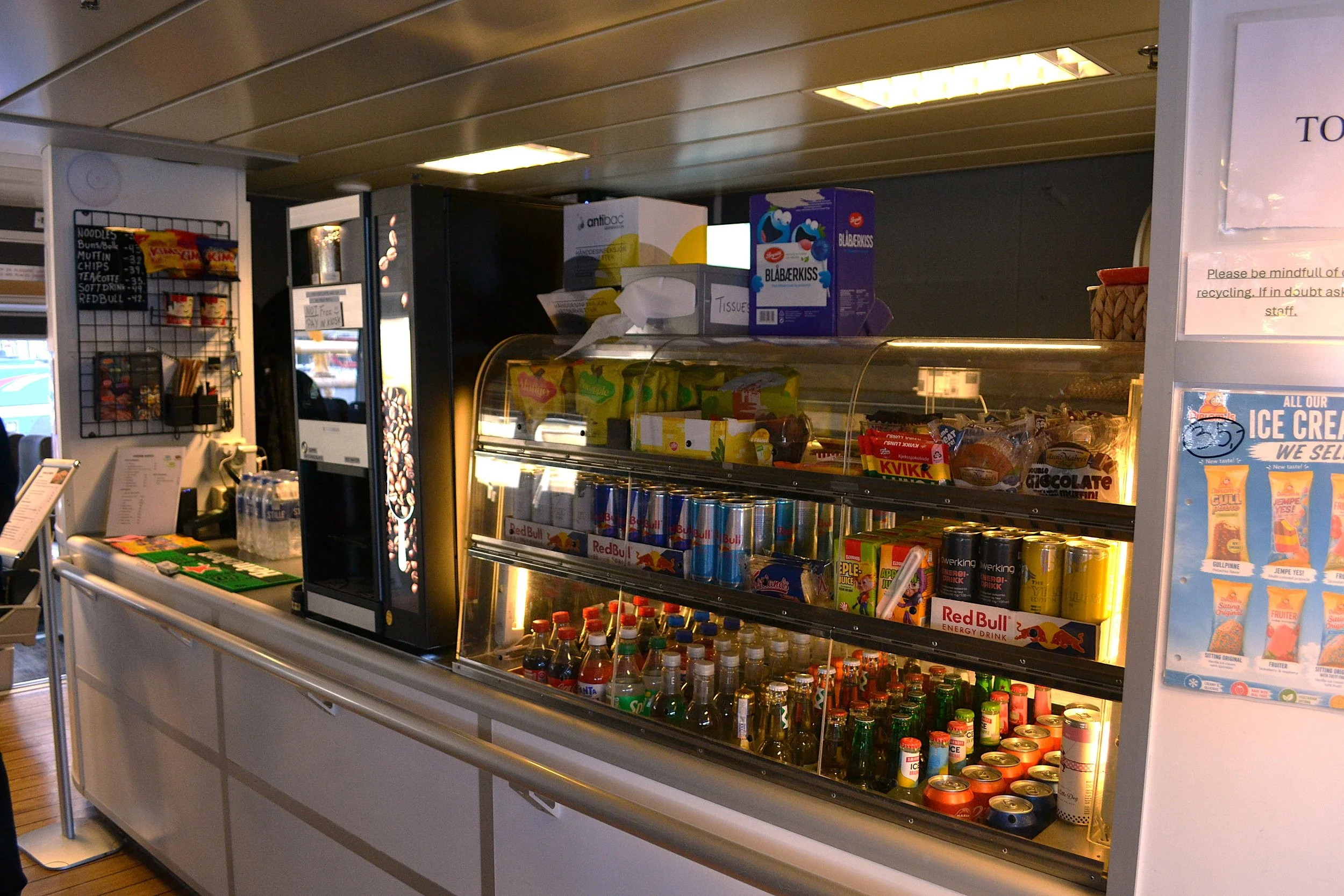 En kioskdisk med ulike drikkevarer og snacks. Det er en kjøledisk med brus og energidrikker.